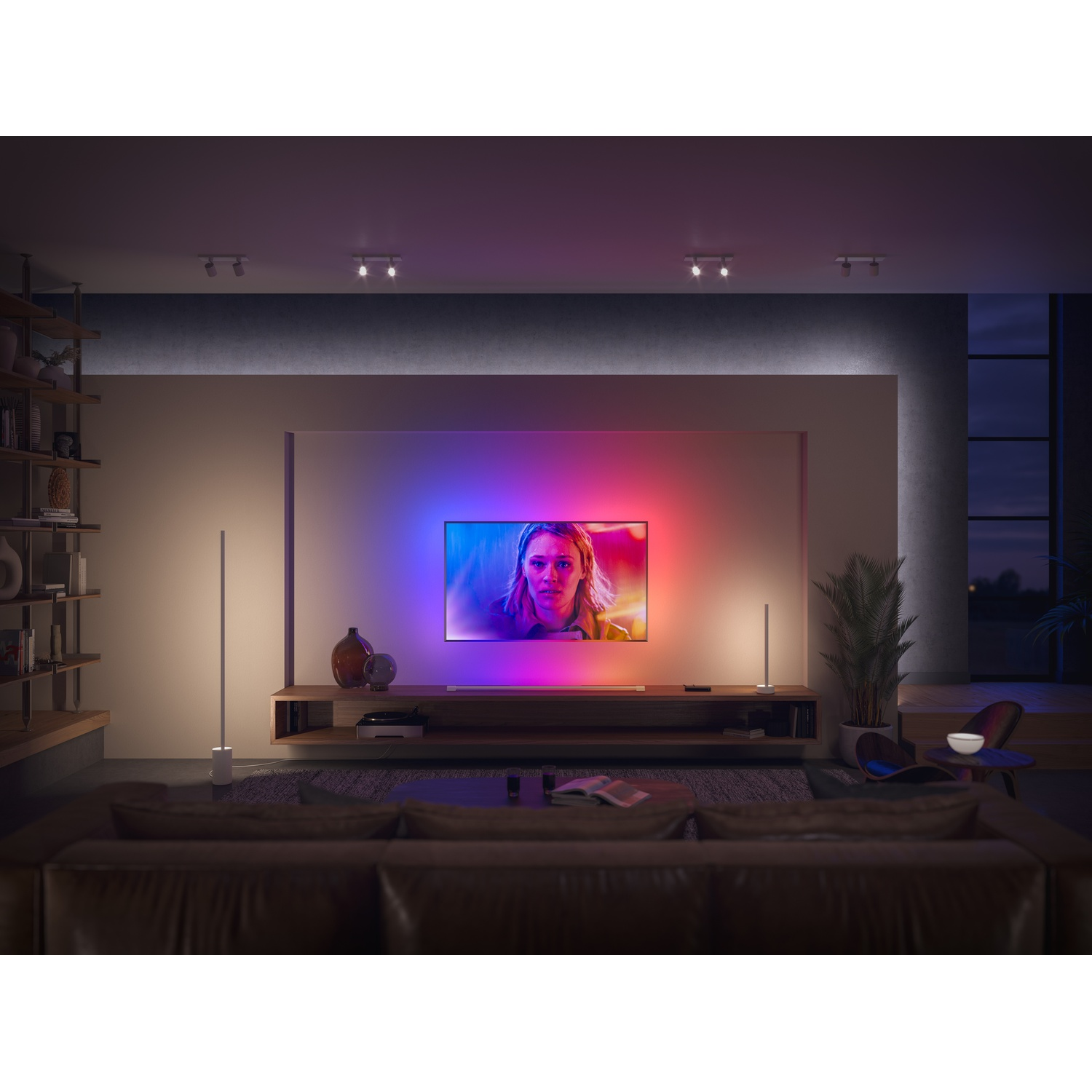 Un soggiorno con una grande TV che mostra il volto di una donna. C'è un divano marrone, lampade da terra e una mensola in legno con decorazioni.