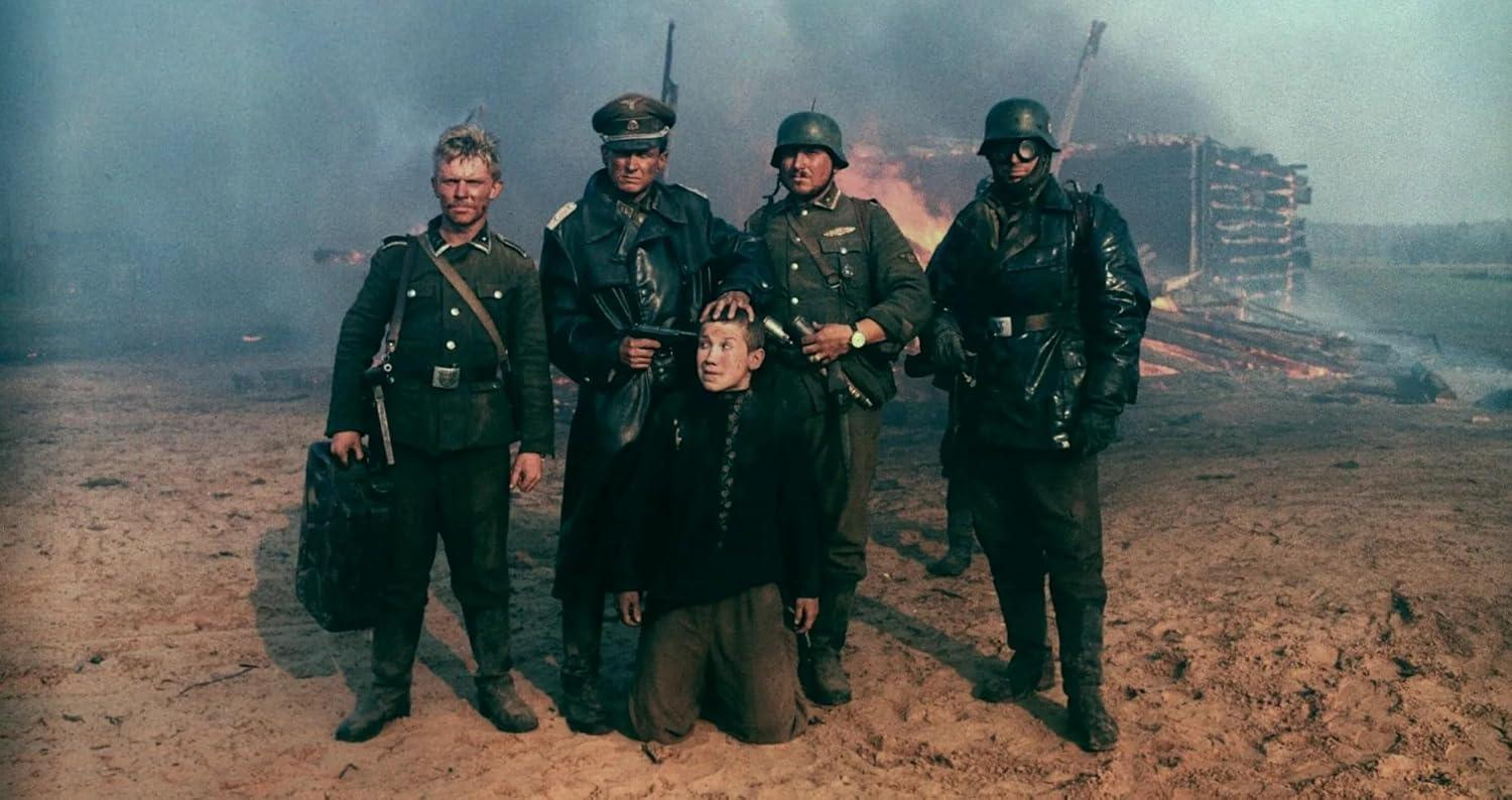 Soldaten umgeben einen knienden Mann. Im Hintergrund brennt ein Gebäude. Die Szene spielt sich auf sandigem Boden mit Rauch ab.