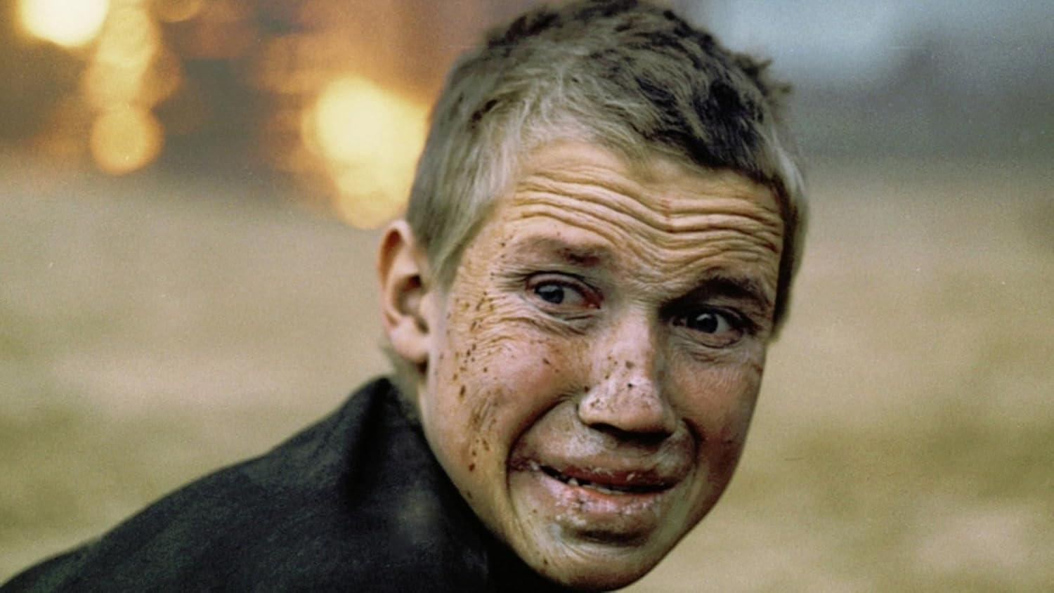 Nahaufnahme eines Mannes mit schmutzbedecktem Gesicht und schmerzverzerrtem Ausdruck. Seine Haare sind kurz und unordentlich, seine Augen zeigen Not.