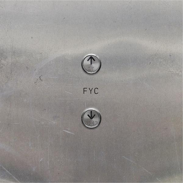Aufzugsknöpfe auf einer gebürsteten Metalloberfläche. Pfeile nach oben und unten sind sichtbar, mit den Buchstaben 'FYC' unter dem Pfeil nach oben.