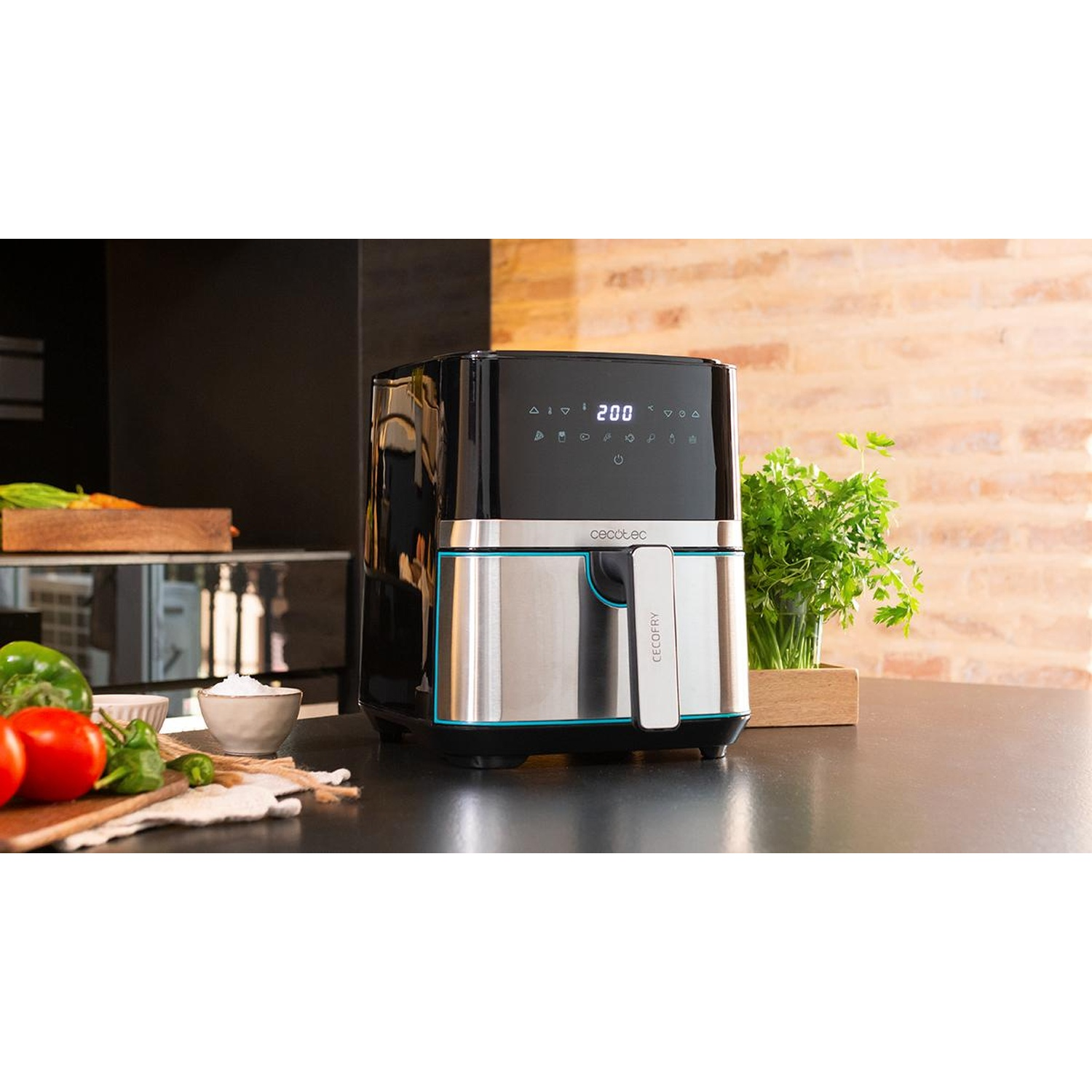 Una friggitrice ad aria con display digitale è su un piano nero. Verdure ed erbe aromatiche sono accanto.