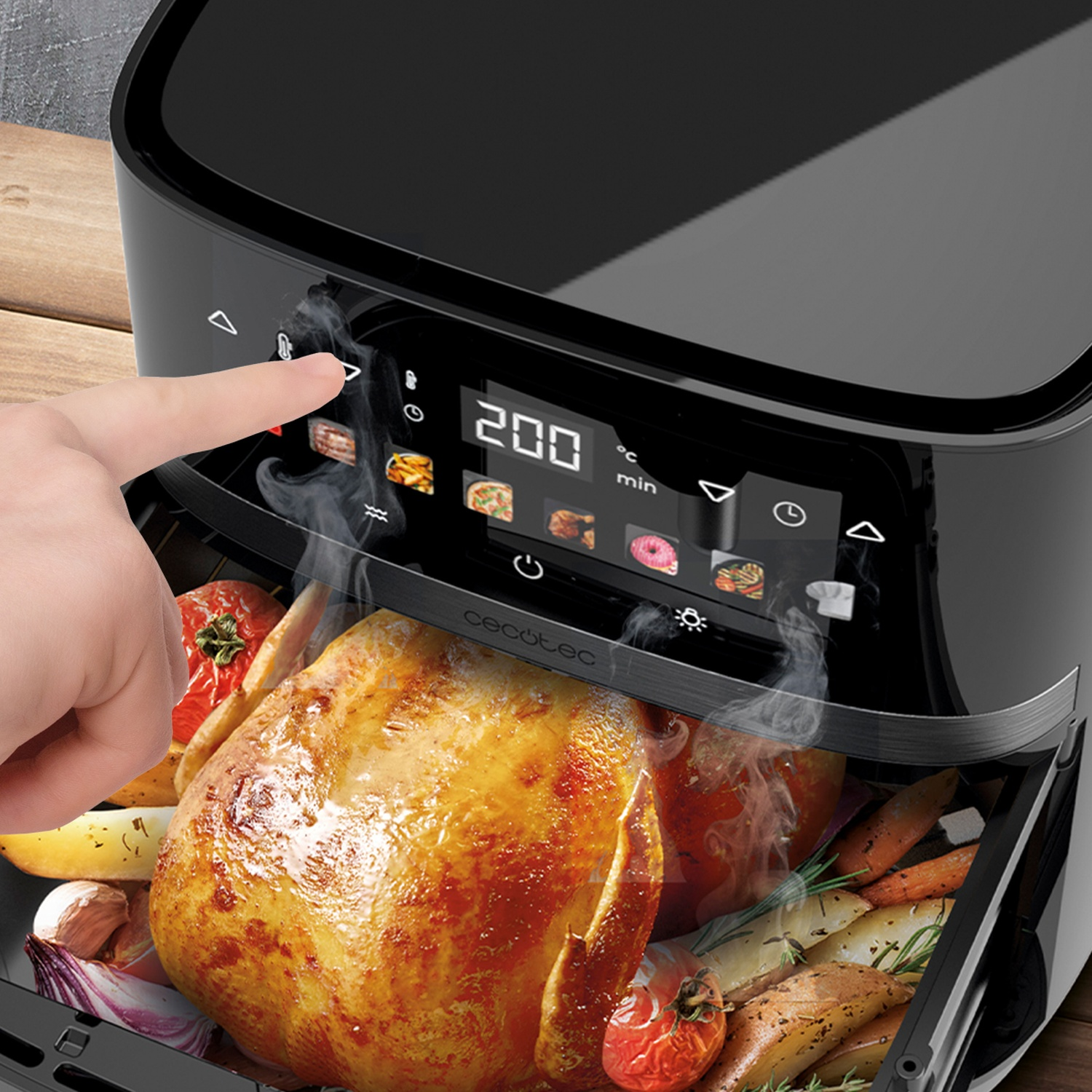 Una mano preme un pulsante della friggitrice ad aria. All'interno c'è un pollo arrosto e verdure, esce vapore. Il display mostra 200 gradi.