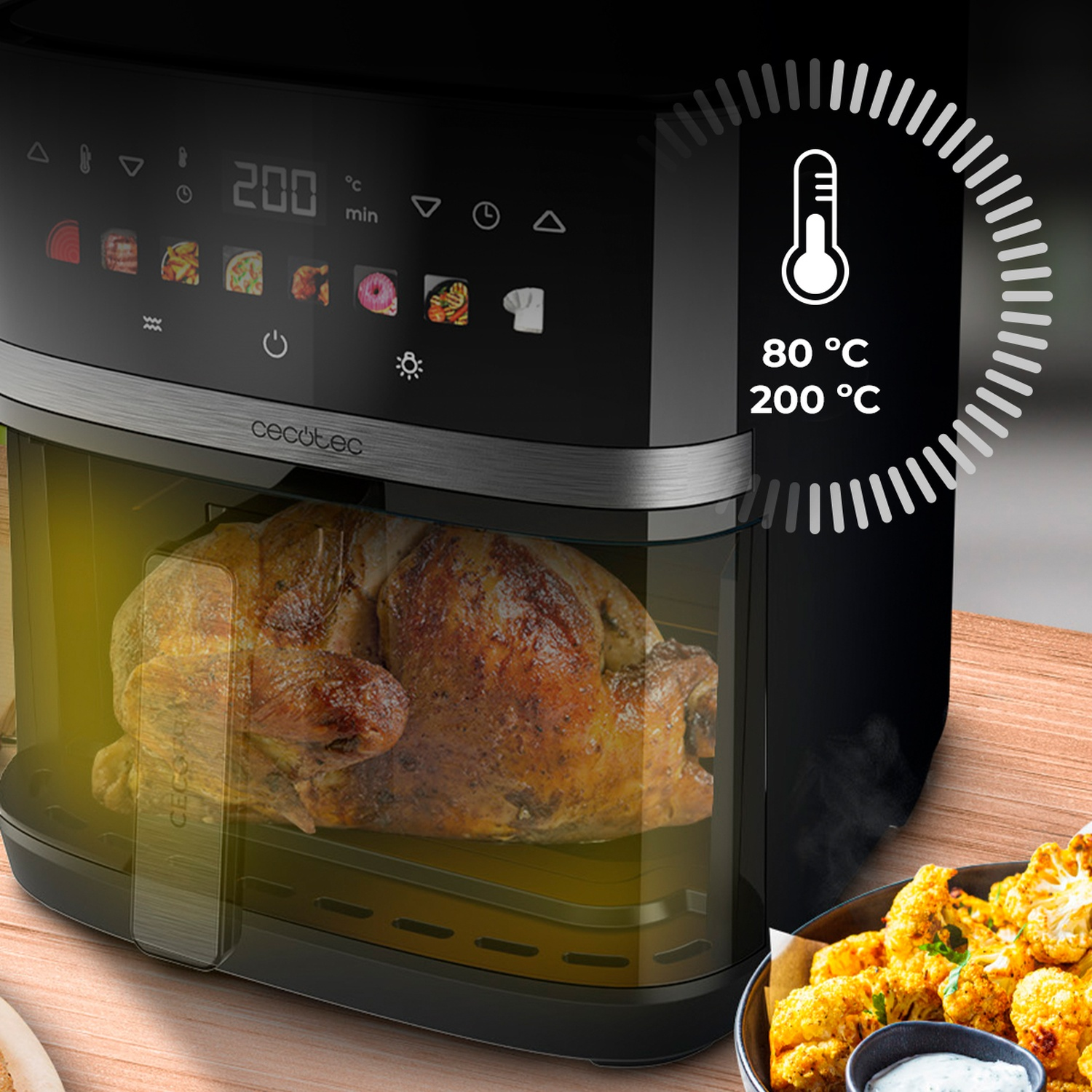 Una friggitrice ad aria con un pollo arrosto all'interno. Il display mostra 200 gradi. Cavolfiore e salsa in primo piano.