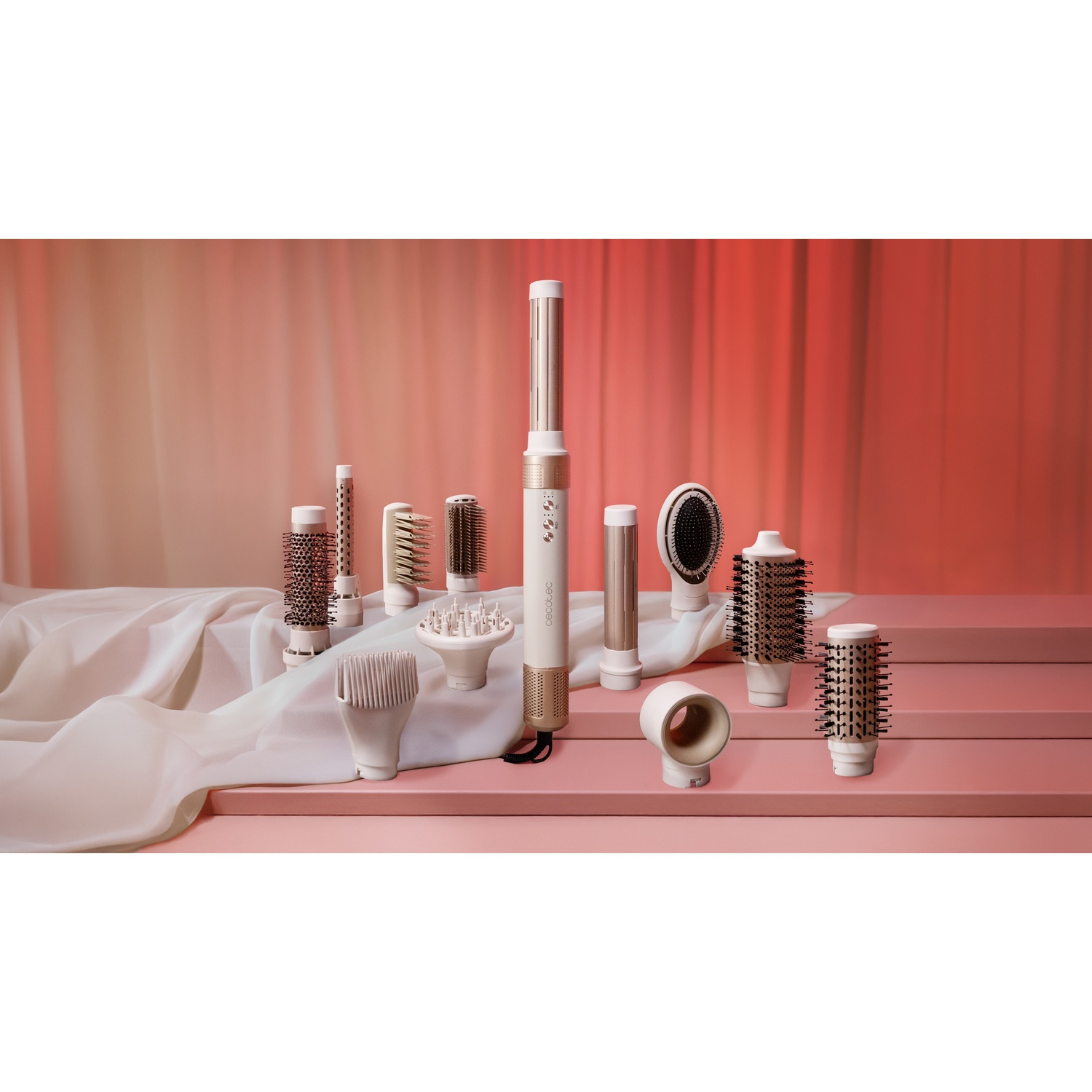 Strumenti per lo styling dei capelli su una superficie rosa. Un asciugacapelli e diversi accessori per spazzole sono esposti su sfondo rosa e bianco.