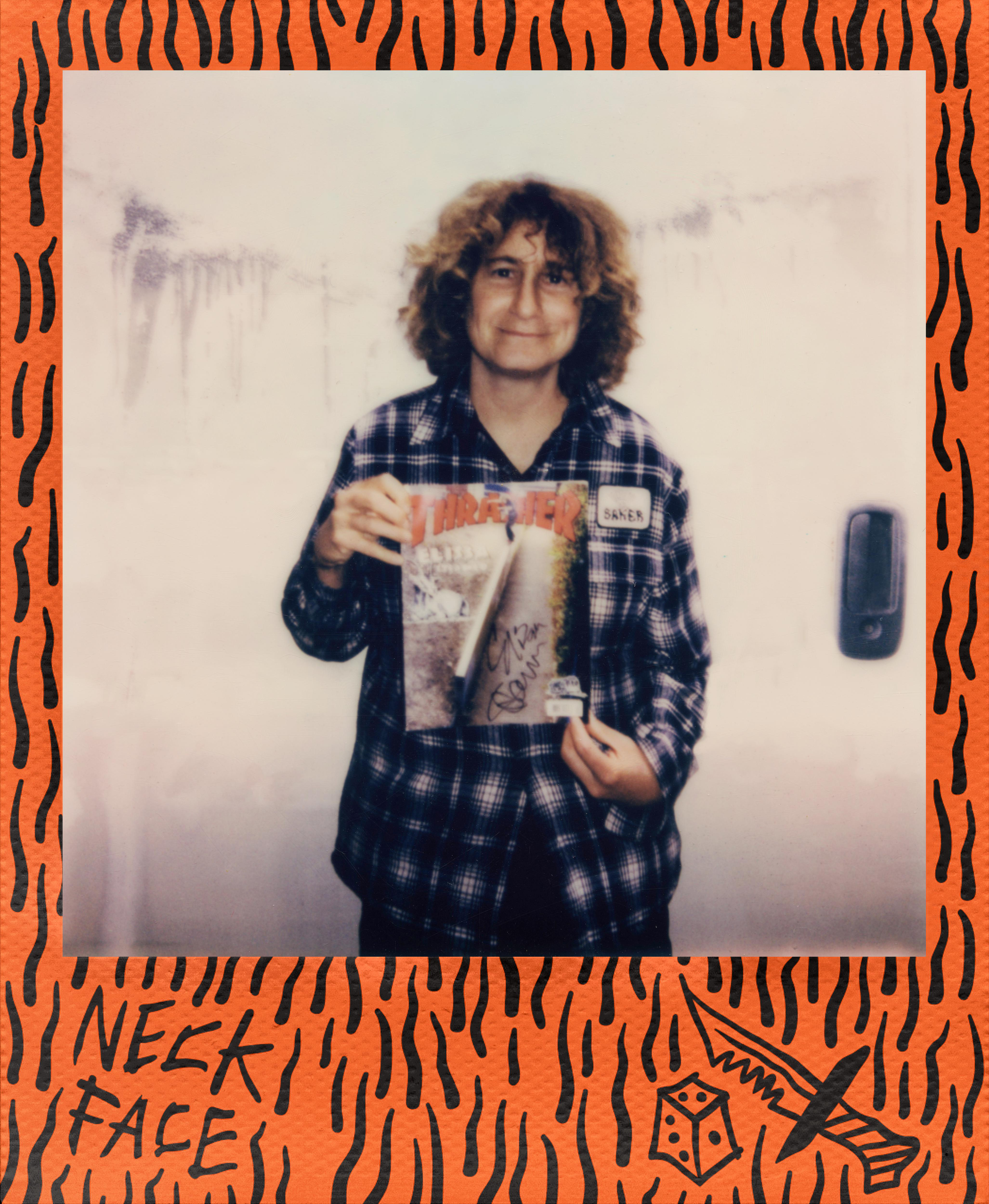 Eine Person hält ein Thrasher-Magazin. Das Polaroid hat einen orangefarbenen Rahmen. Der Hintergrund ist eine weiße Wand.