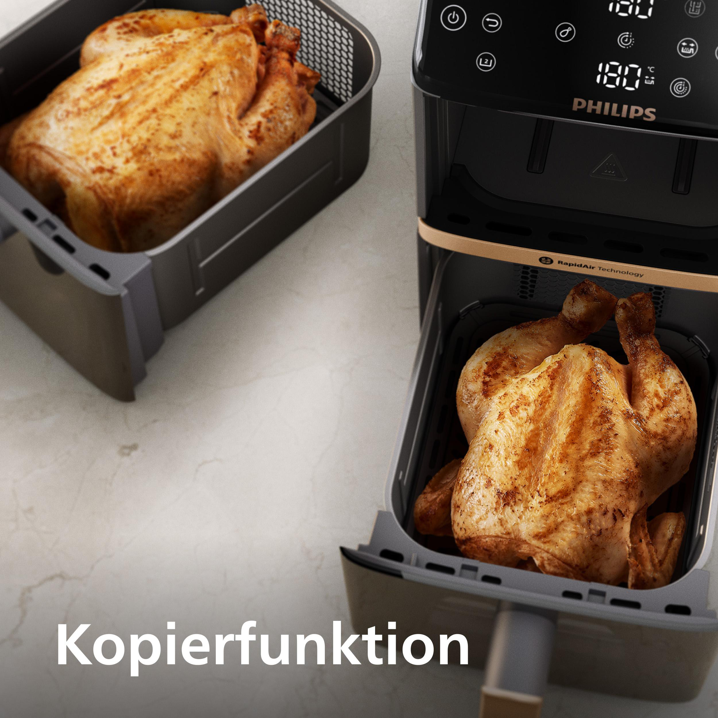 Ein Heißluftfritteuse mit zwei gebratenen Hähnchen. Die Fritteuse ist schwarz. Der Hintergrund ist eine hellgraue Oberfläche.