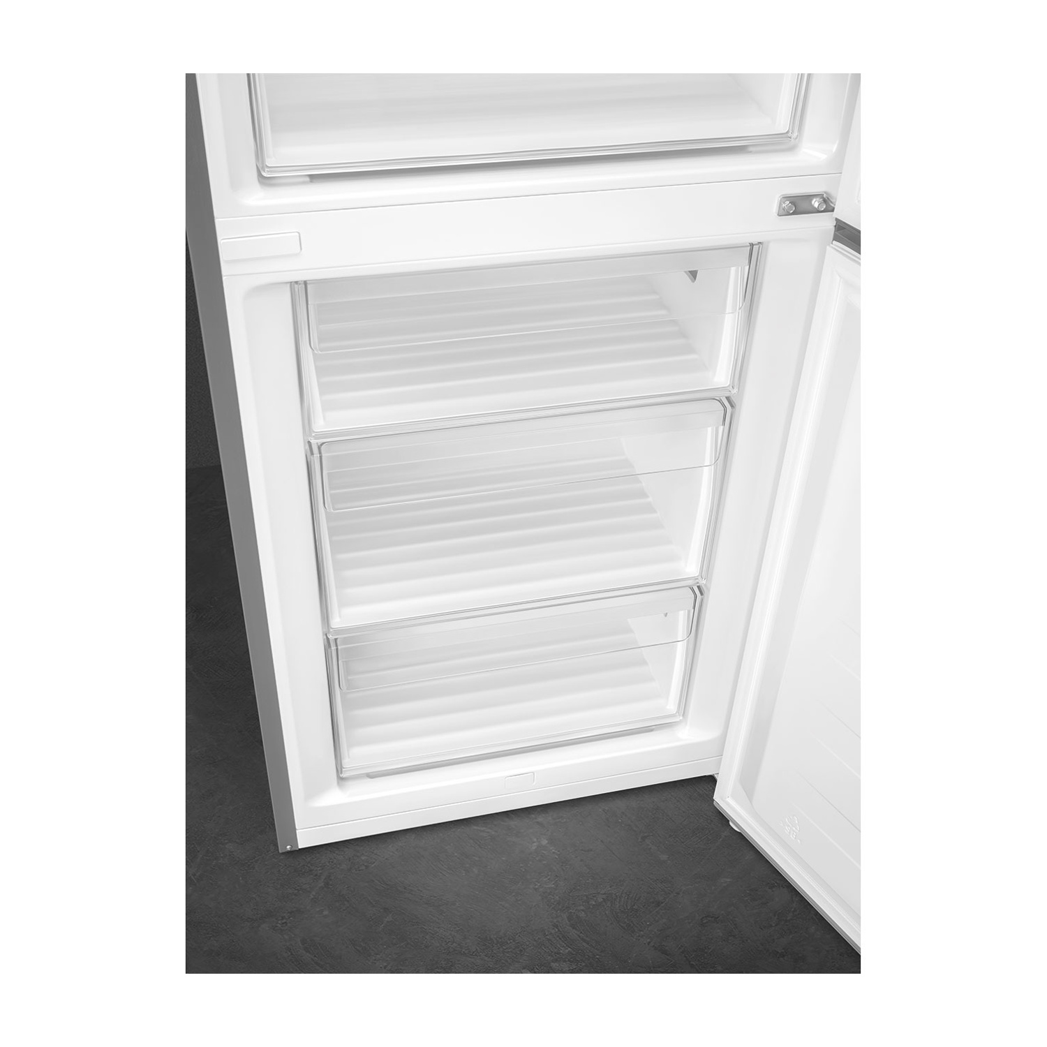 Un frigorifero bianco con la porta del congelatore aperta, che rivela tre cassetti trasparenti. La porta è leggermente socchiusa. Pavimento scuro.