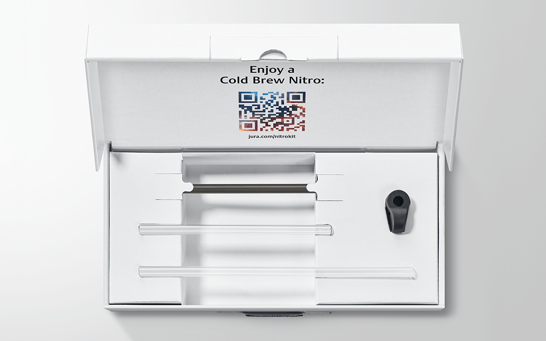 Geöffnete weiße Box mit Fächern, die Glasröhren und eine schwarze Kunststoffkomponente enthalten. QR-Code und Text 'Enjoy a Cold Brew Nitro'.