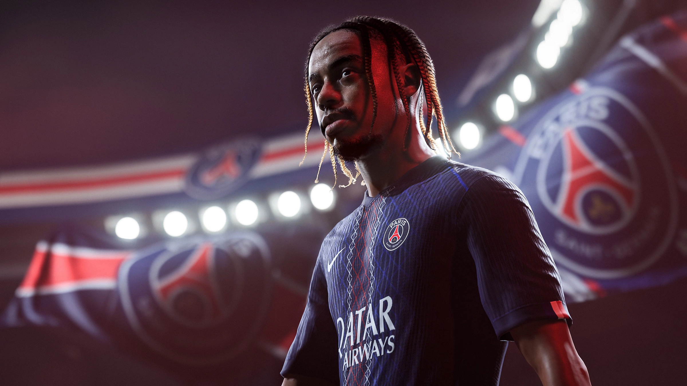 Un calciatore con una maglia blu è in uno stadio. La maglia ha i loghi degli sponsor. Lo sfondo mostra il logo della squadra.