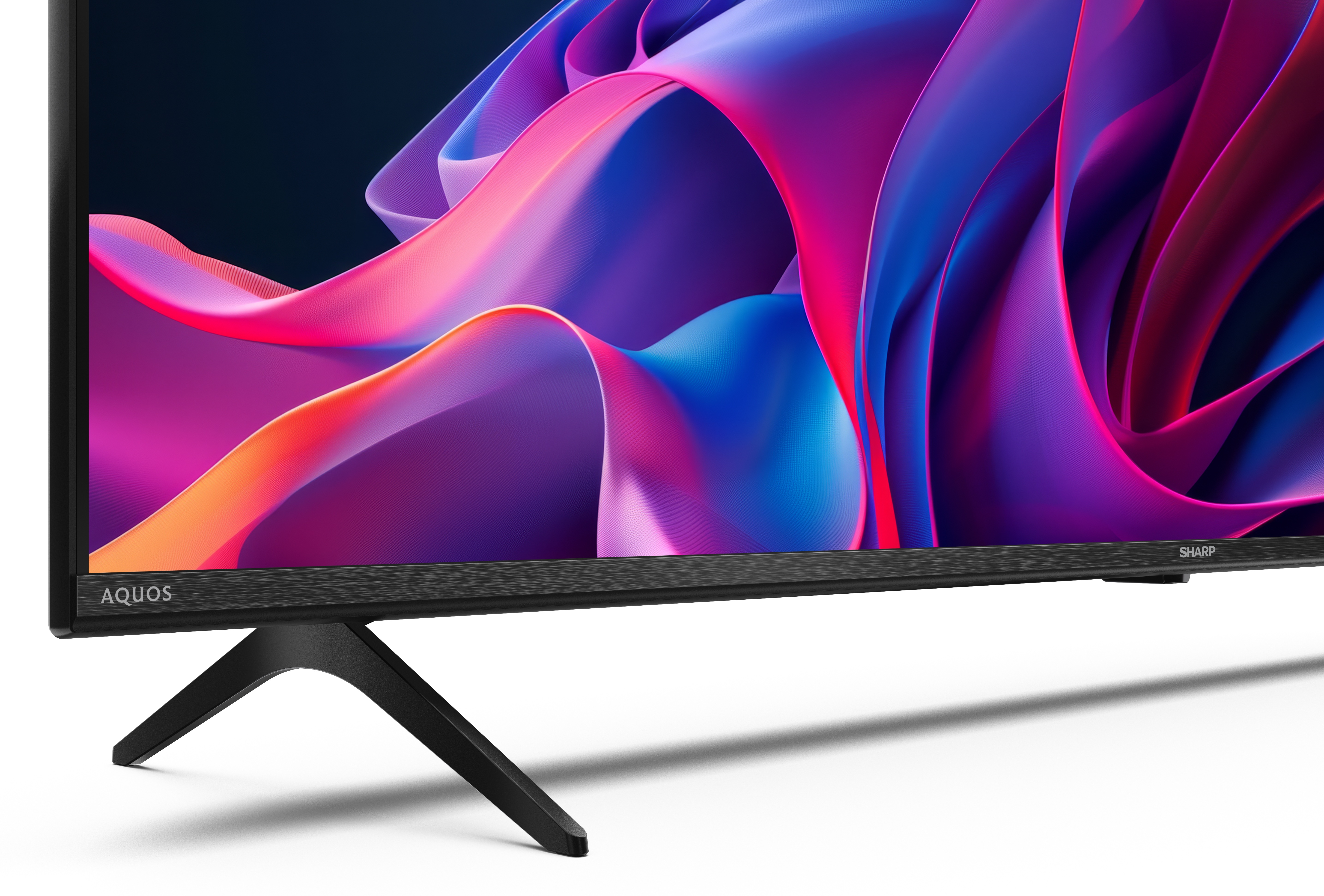 Czarny telewizor Sharp Aquos z kolorowym, abstrakcyjnym wyświetlaczem na czarnym stojaku na białym tle.