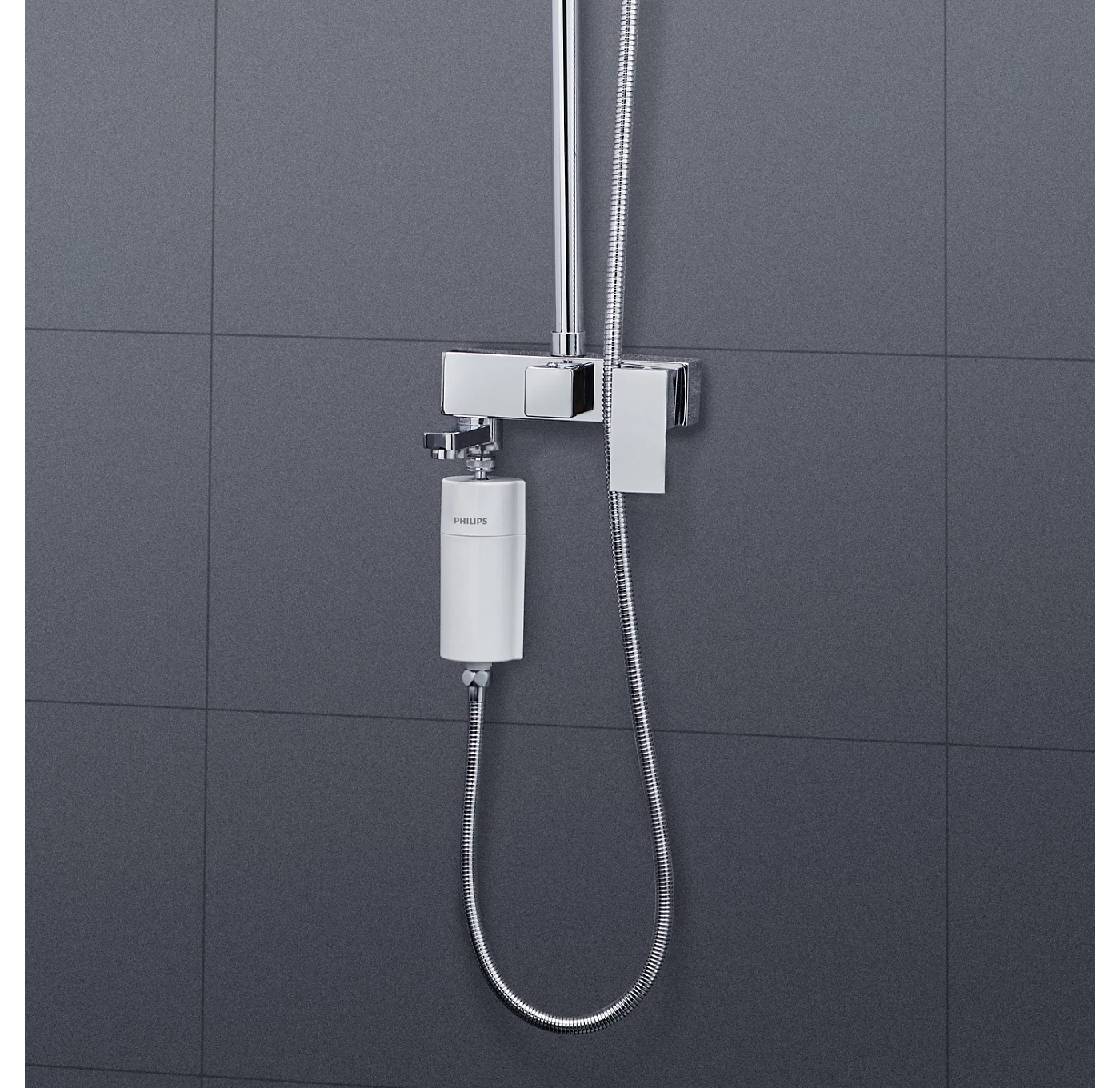 Egy króm zuhanyfej és csaptelep egy szürke csempézett falra van szerelve. Egy fehér vízszűrő Philips logóval van rögzítve.