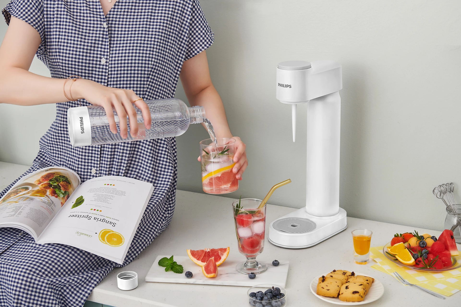 Egy nő vizet önt egy üvegből grapefruit-tal és jéggel. A közelben egy fehér italautomata áll.