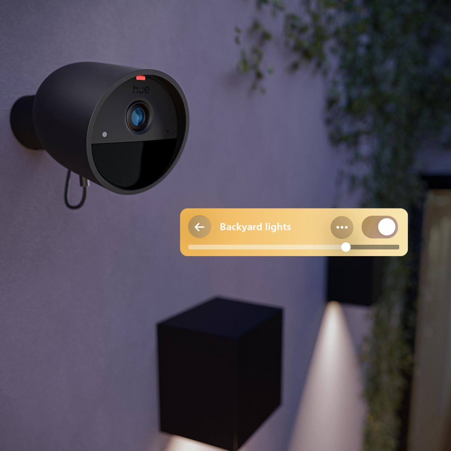 A black security camera on a wall, with a 'Backyard lights' control panel overlayed. Two black cube lights are below.