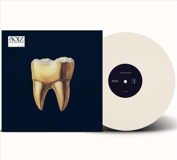 Albumcover mit einem Goldzahn auf dunklem blauem Hintergrund, neben einer weißen Schallplatte.