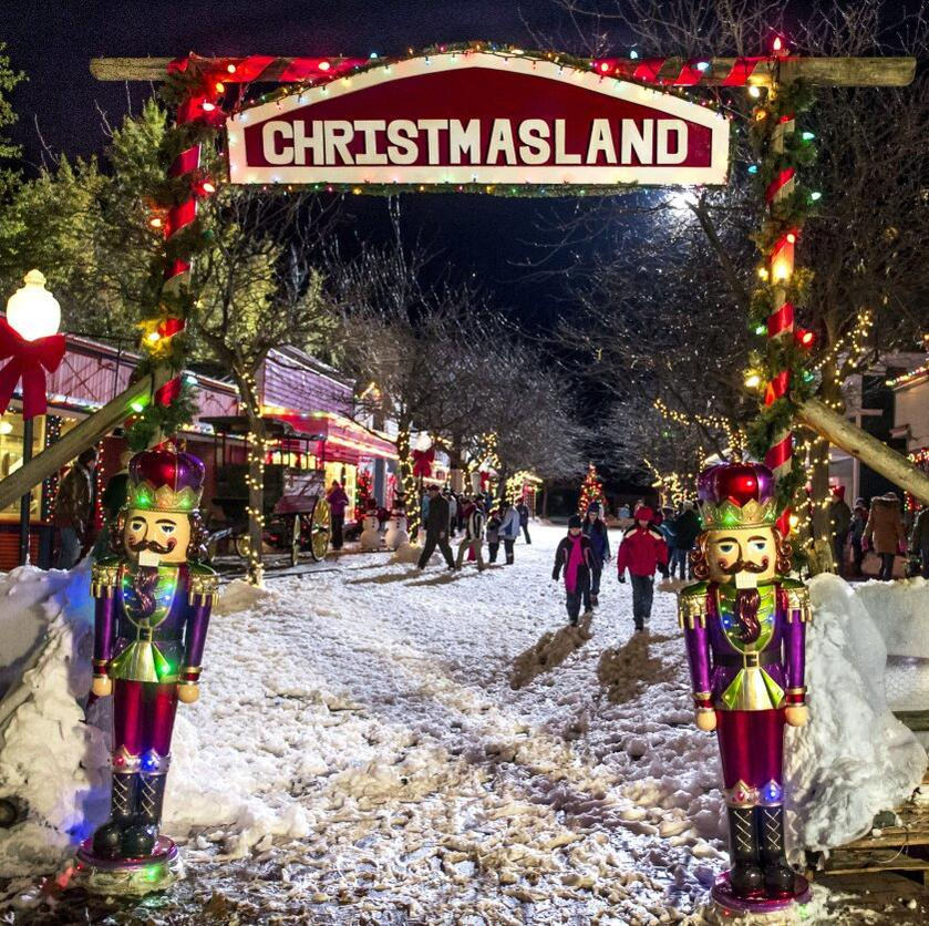 Nächtliche Szene in Christmasland. Ein Schild sagt 'Christmasland'. Zwei Nussknacker-Statuen stehen am Eingang. Menschen gehen auf Schnee.