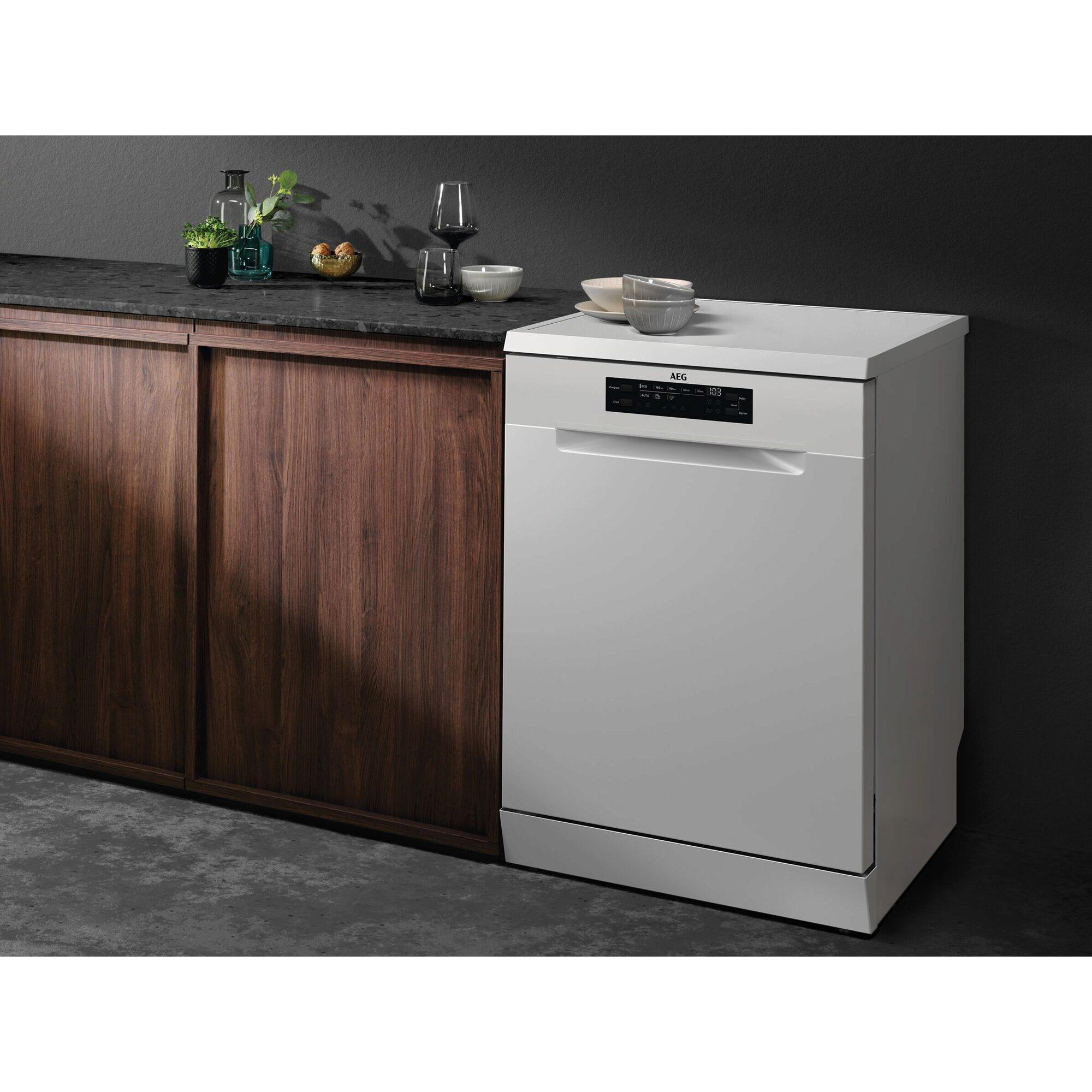 Eine weiße AEG-Spülmaschine neben einem dunklen Holzschrank. Schalen, Gläser und Pflanzen stehen auf der Arbeitsplatte.