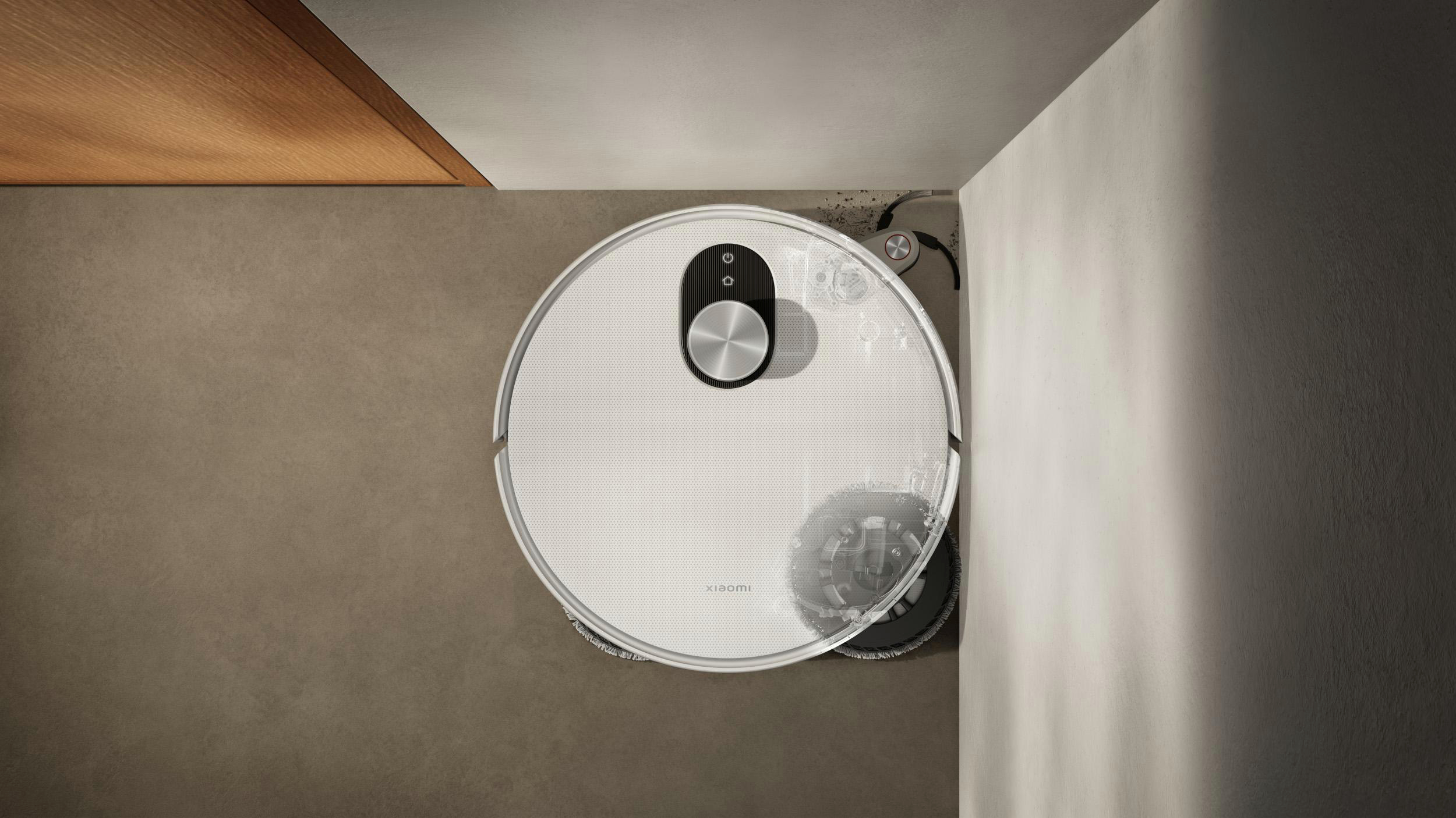 Ein weißer Xiaomi-Roboter-Staubsauger auf einem braunen Boden, in der Nähe einer Wand. Der Staubsauger ist rund. Boden und Wand sind im Hintergrund.