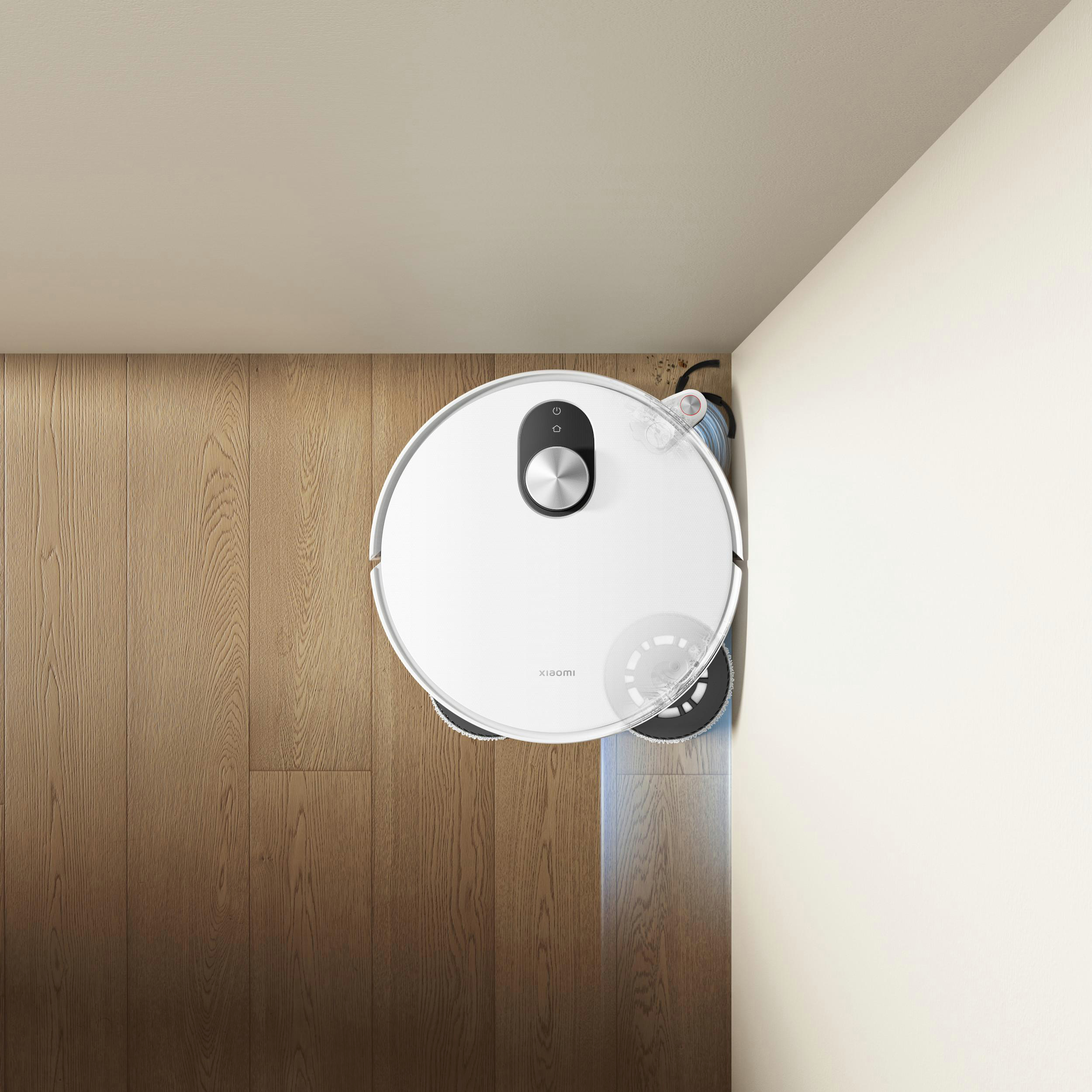 Ein weißer Roboter-Staubsauger reinigt einen Holzboden neben einer weißen Wand.