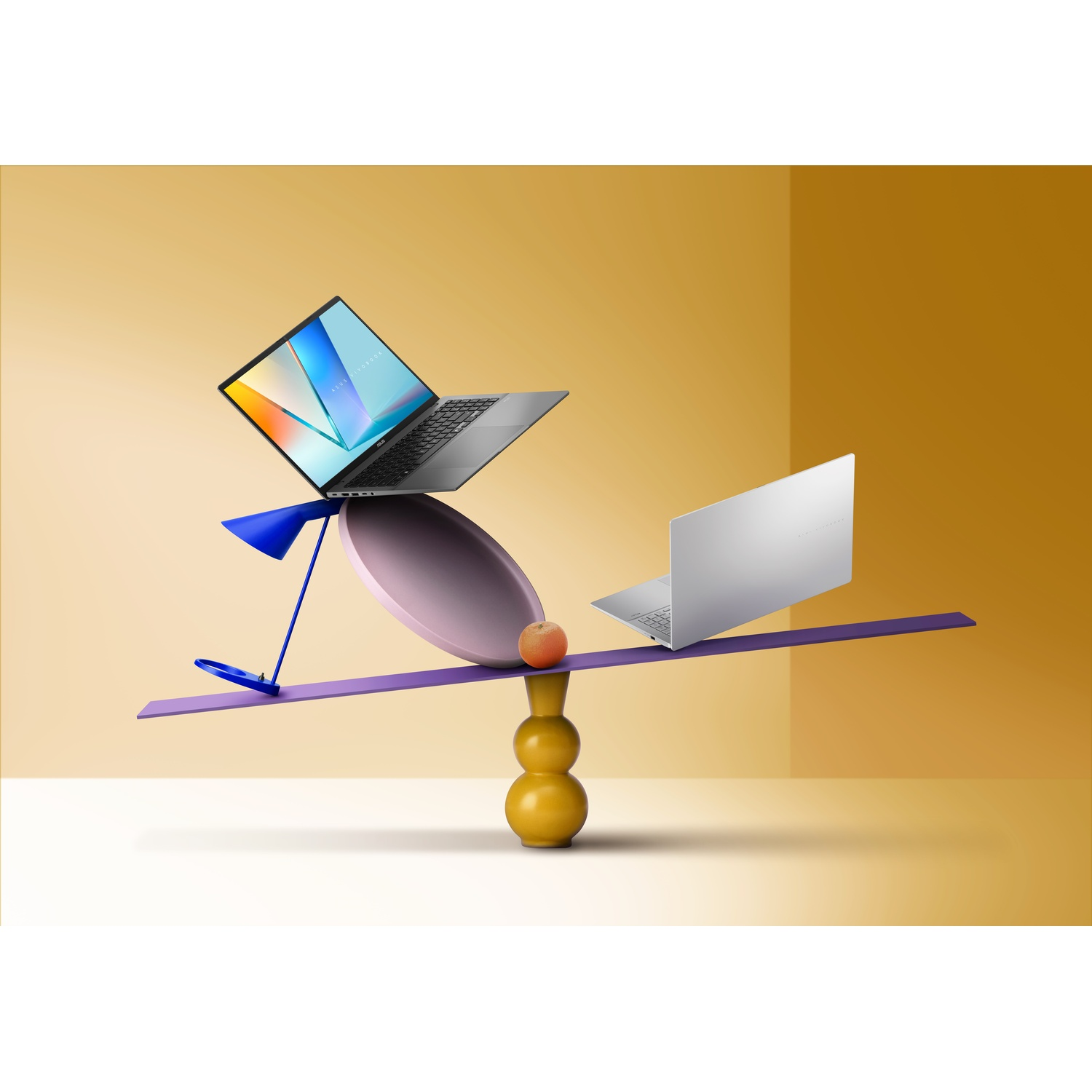 Due laptop in equilibrio su un'altalena viola con una pesca. Sono presenti anche una lampada blu e un vaso giallo.