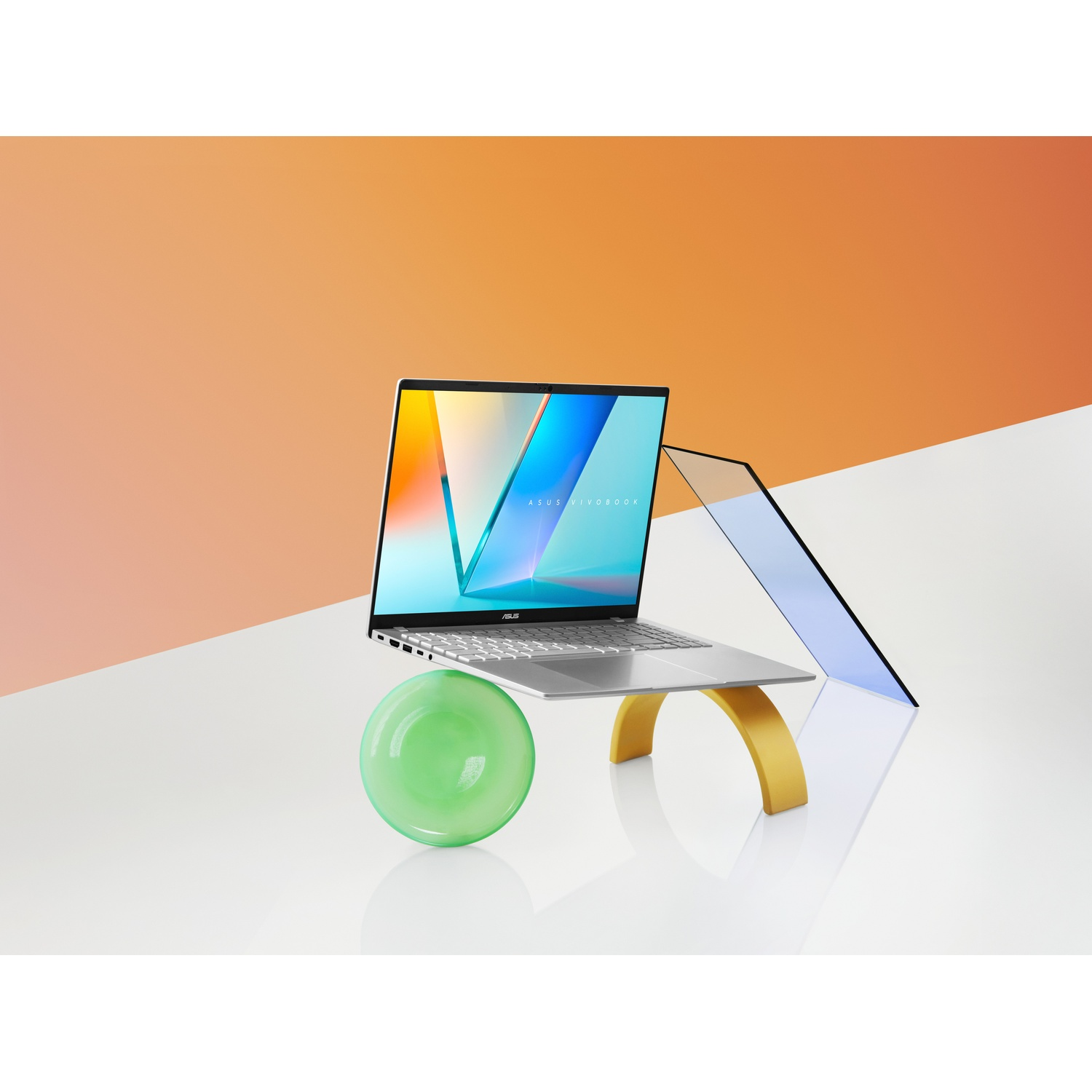Un laptop su un supporto. Il laptop ha uno schermo colorato. Dietro, una forma di vetro e uno sfondo arancione e bianco.