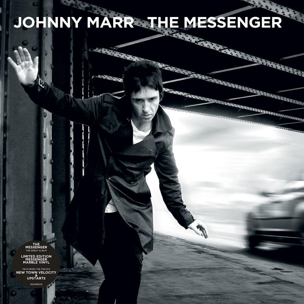 Johnny Marr lehnt sich an eine Brücke, Arm ausgestreckt. Ein verschwommenes Auto fährt im Hintergrund vorbei. Albumtitel: The Messenger.