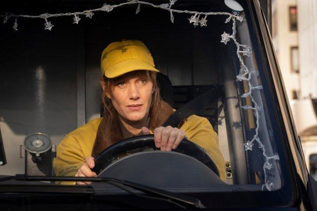 Eine Frau in gelber Mütze und Jacke fährt einen Lkw. Sterne leuchten auf der Windschutzscheibe. Die Frau schaut nach vorne.