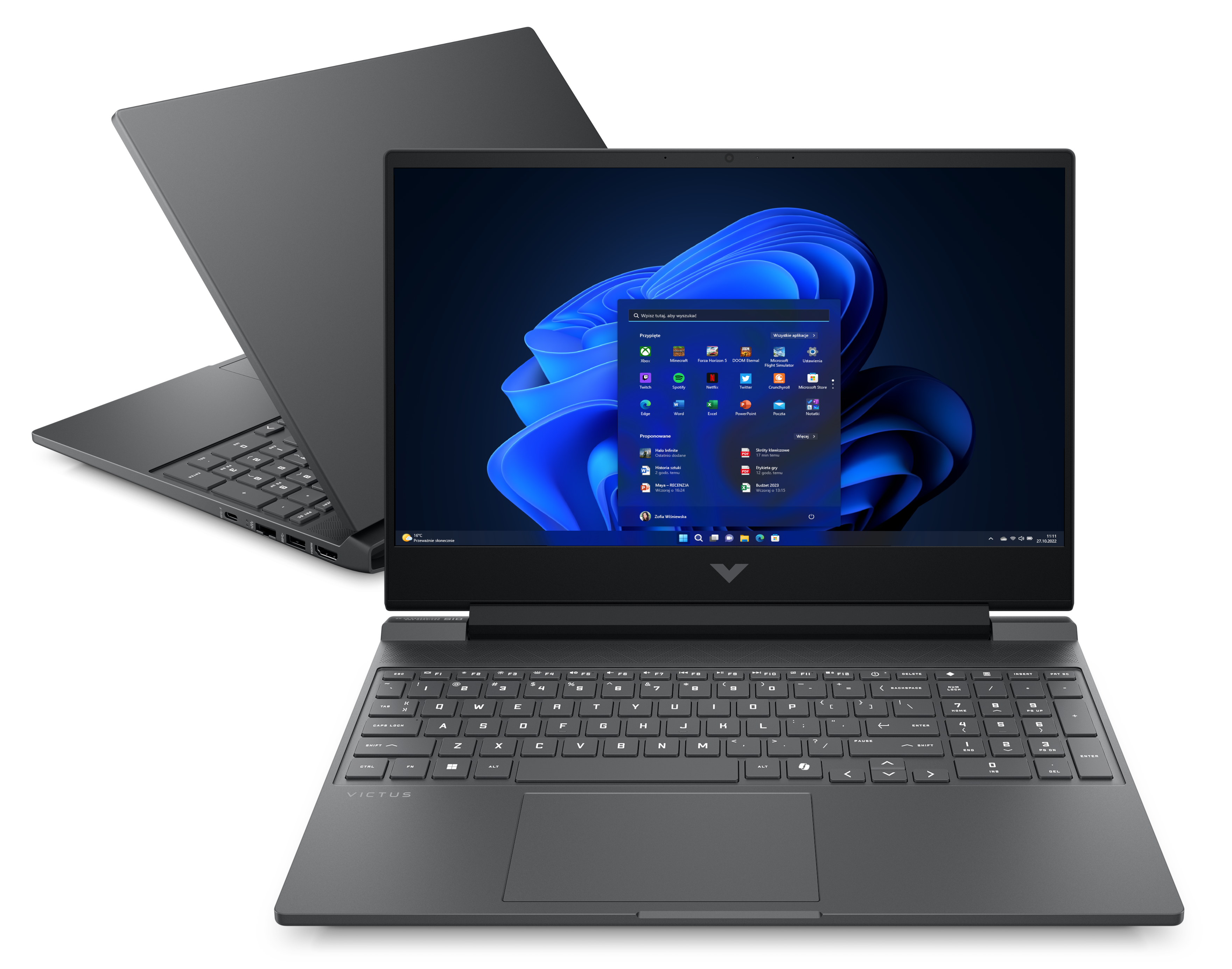 Ciemnoszary laptop jest otwarty, wyświetlając interfejs Windows 11. Drugi laptop jest lekko z tyłu.