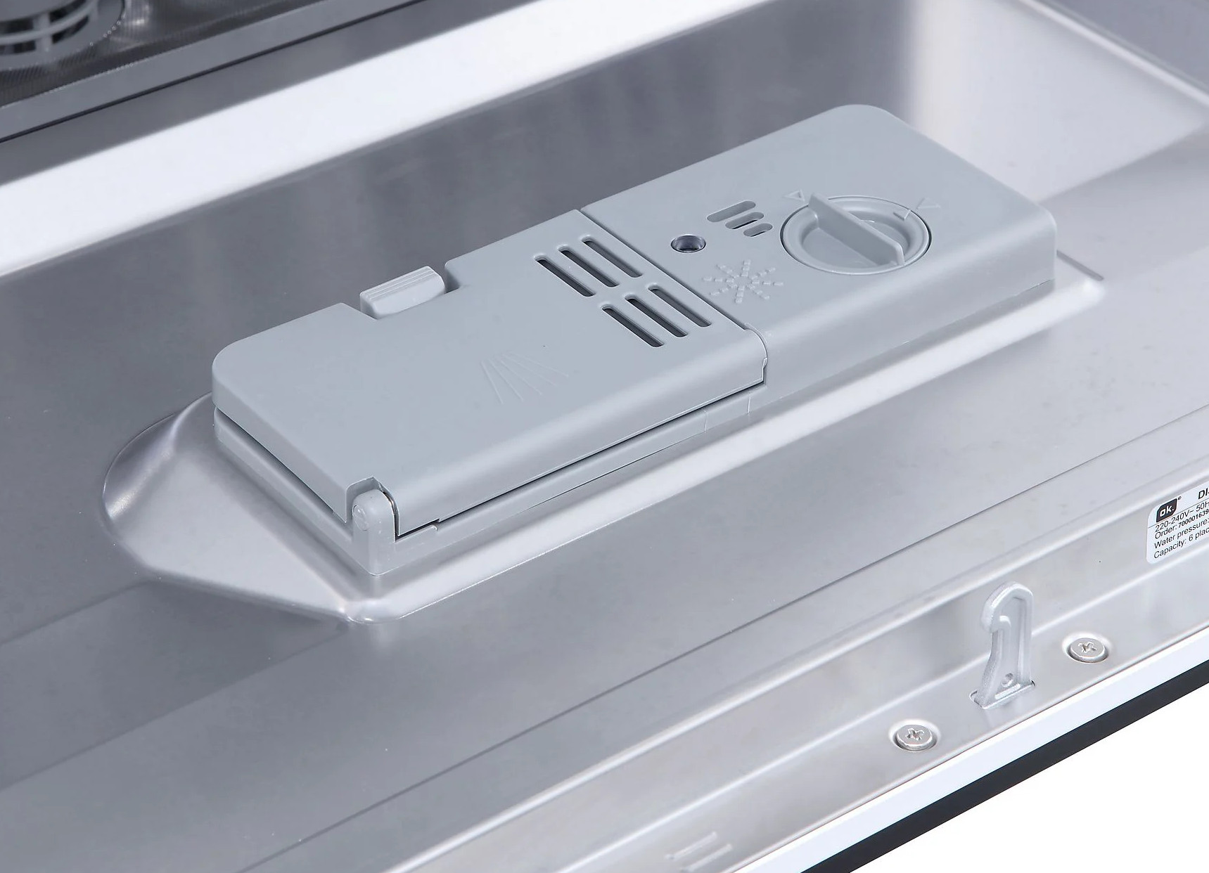 Zbliżenie dozownika detergentu zmywarki. Ma jasnoszary kolor. Dozownik jest otwarty.