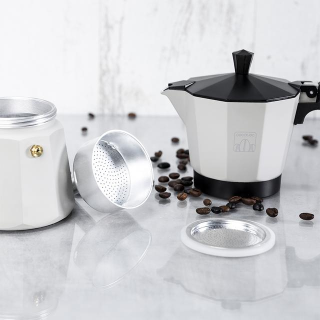 Una cafetera blanca y negra desmontada con granos de café esparcidos. Incluye base, filtro y tapa.