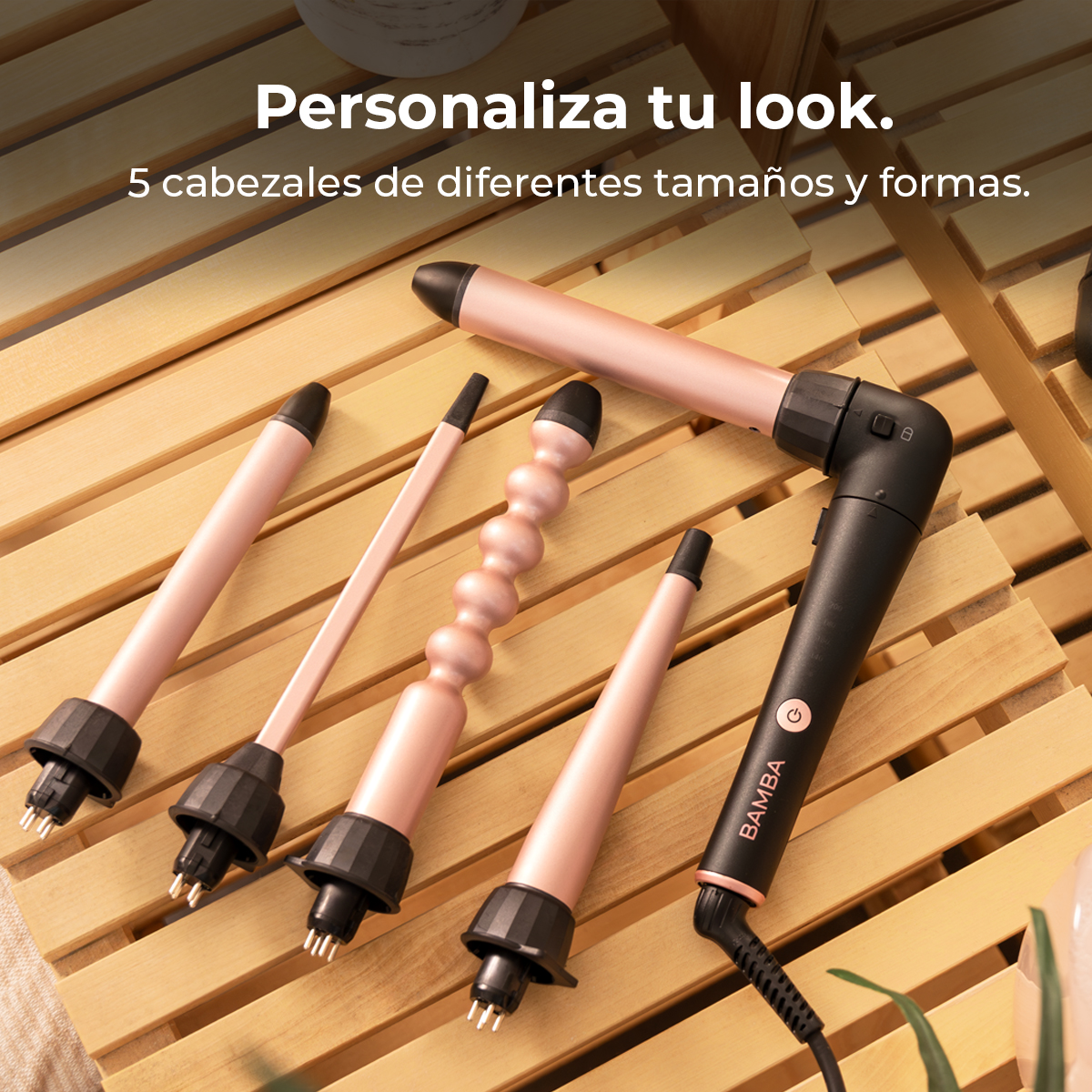 Cinco cabezales rizadores oro rosa con bases negras sobre superficie de madera. Un mango negro con el logotipo Bamba.
