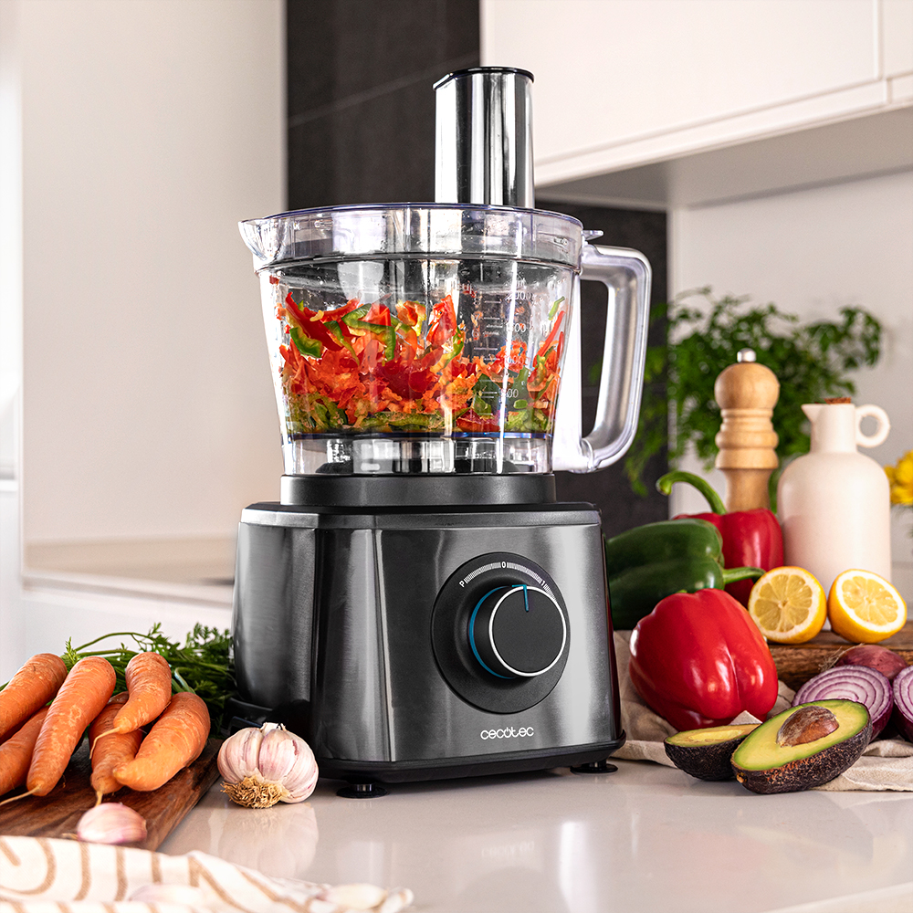 Un procesador de alimentos con pimientos rojos picados. Zanahorias, ajo, aguacate, limones y pimientos en el mostrador.