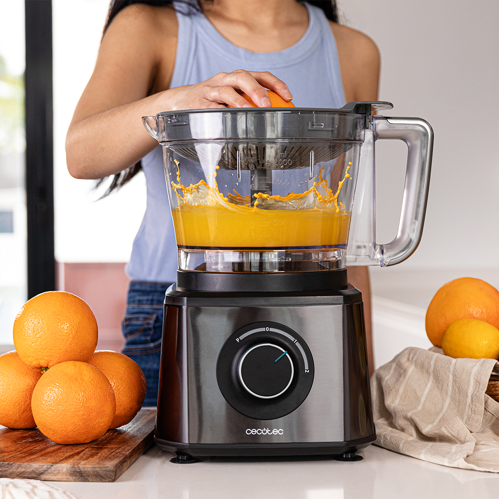 Una persona exprimiendo una naranja con un exprimidor eléctrico. Las naranjas están en una tabla de cortar y junto al exprimidor.