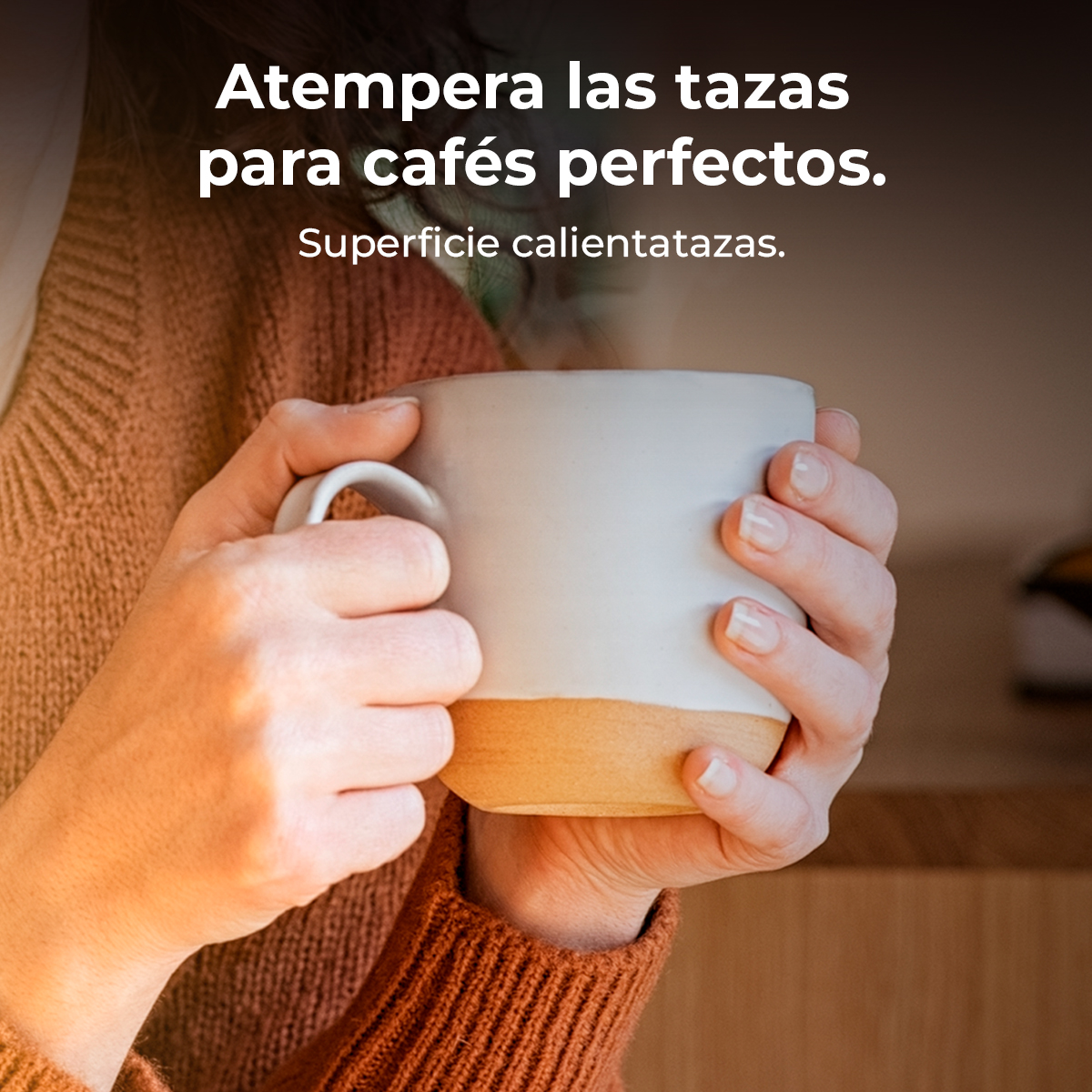 Una persona sostiene una taza de café. La taza es blanca con una base marrón. La persona usa un suéter naranja.