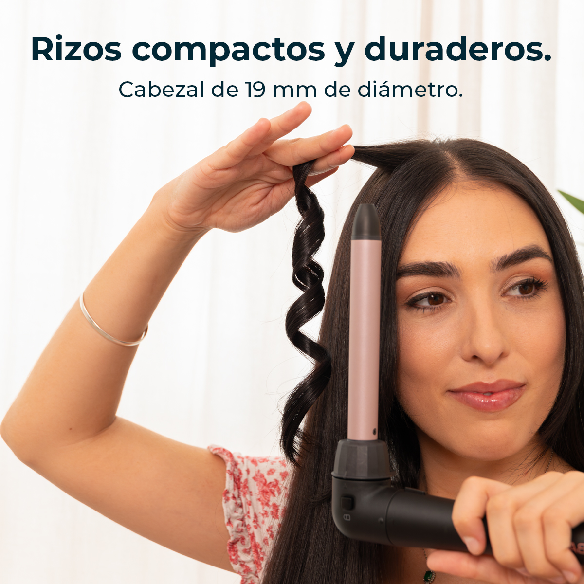 Una mujer con cabello largo y oscuro se riza un mechón con un rizador. El cabello rizado es una espiral apretada. El texto dice 'rizos compactos y duraderos'.