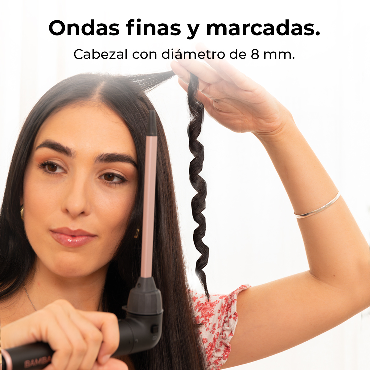 Mujer rizando su cabello con una plancha. Su cabello oscuro está siendo peinado. Lleva una blusa floral y una pulsera plateada.
