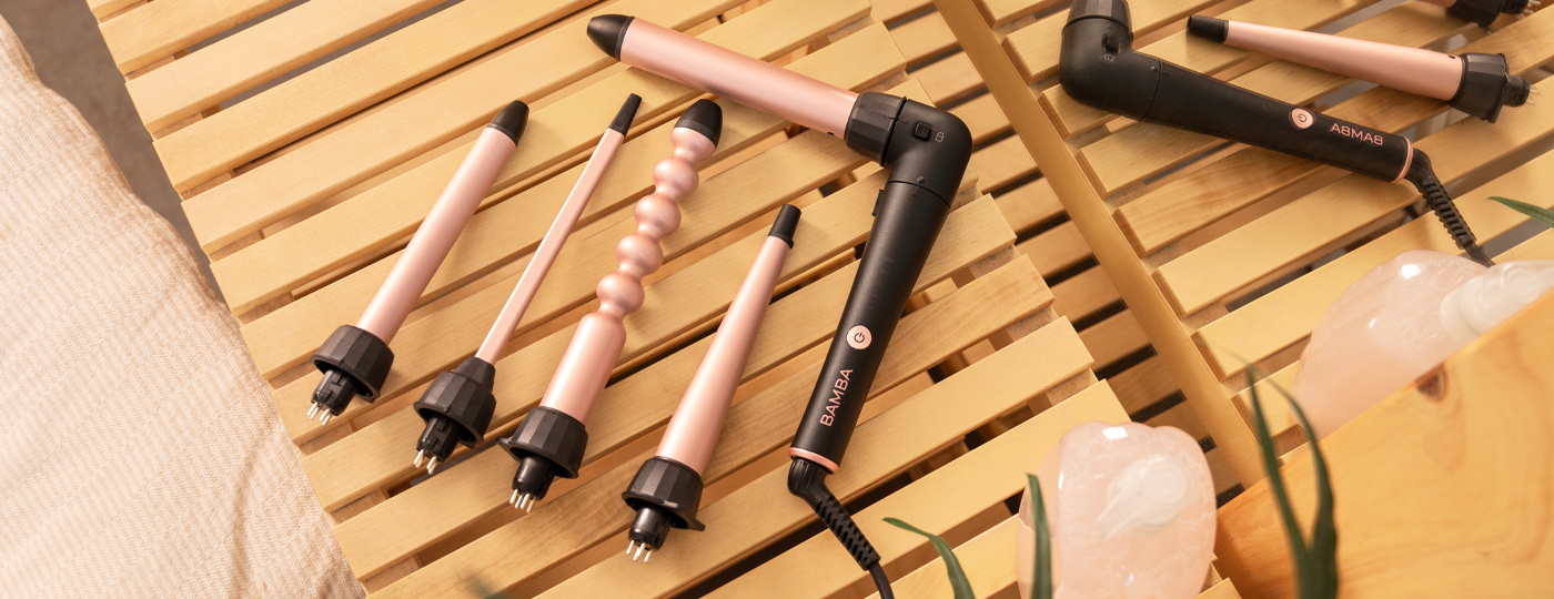 Varias planchas para el pelo sobre una superficie de madera. Diseño negro y oro rosa. Accesorios incluyen una almohada y cristales.