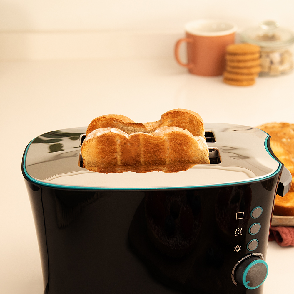 Una tostadora negra con rebanadas de pan tostado. Una taza marrón y galletas en el fondo borroso.