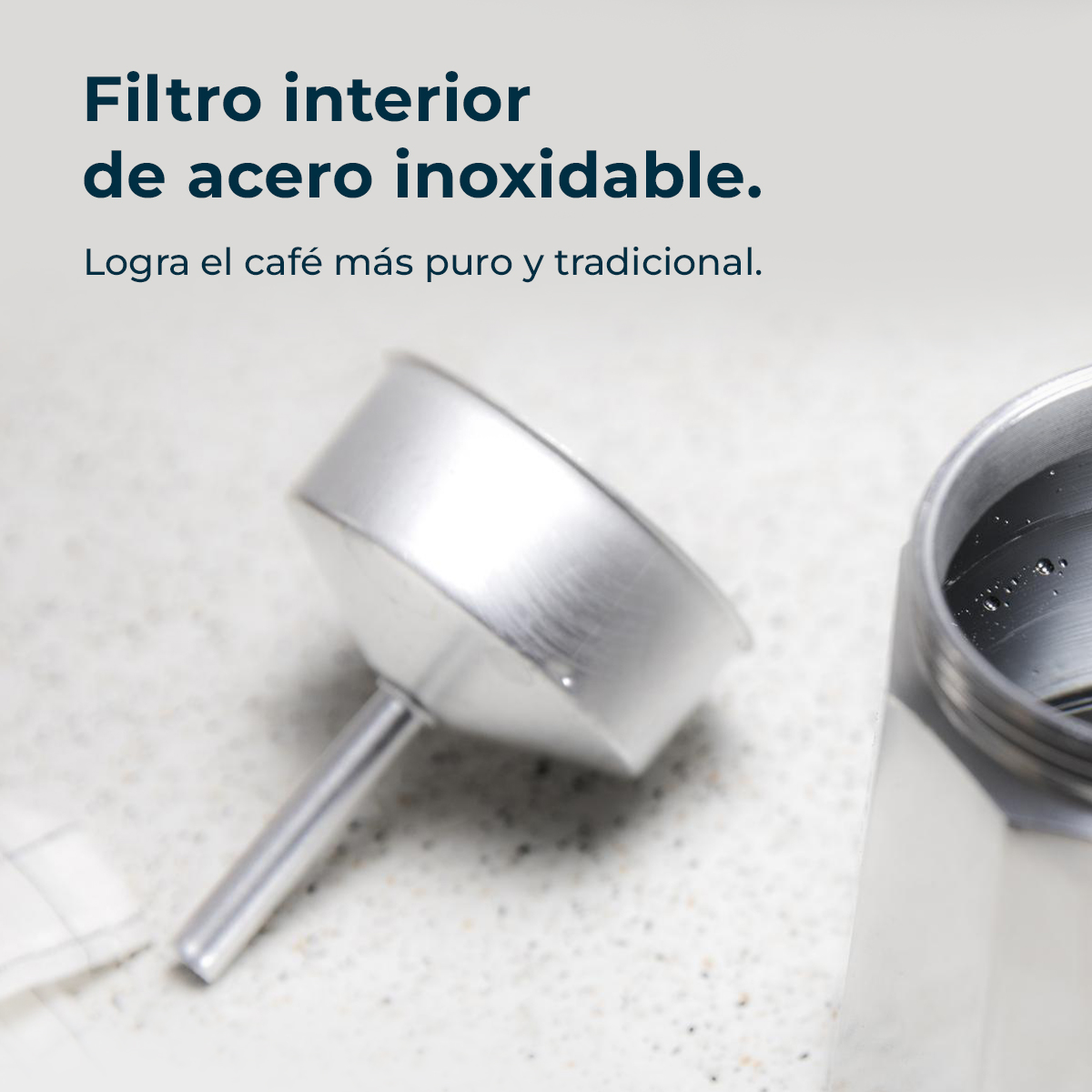 Primer plano de un filtro de café de acero inoxidable y parte de una cafetera. El fondo muestra una encimera de color claro.