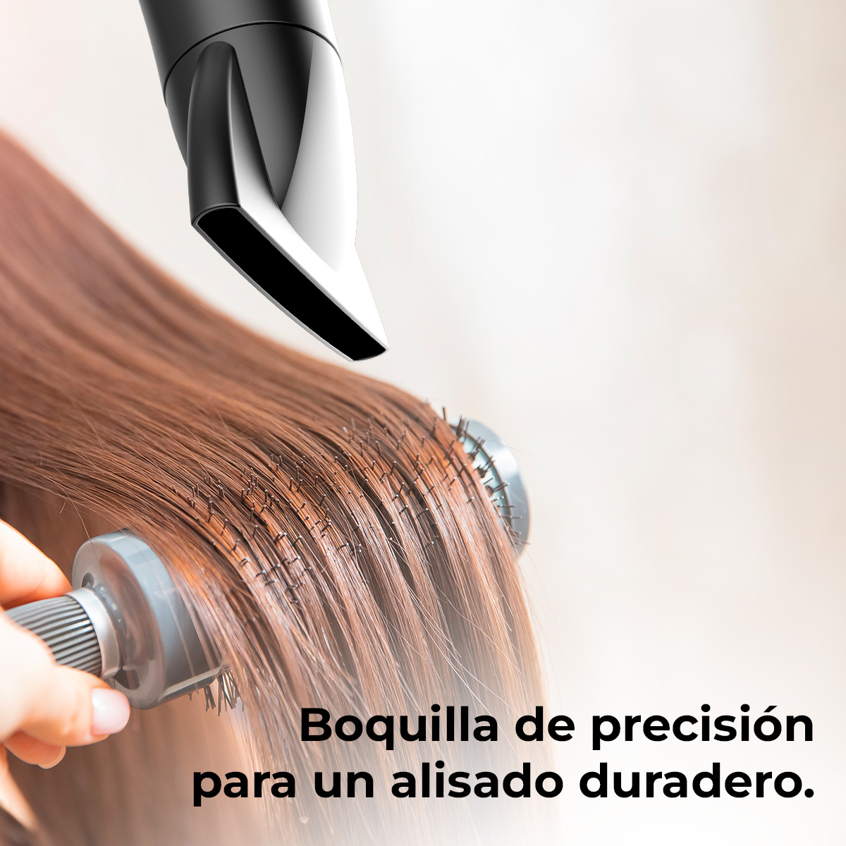 Se usa un secador de pelo con boquilla sobre cabello castaño con un cepillo redondo. El fondo es claro y borroso.