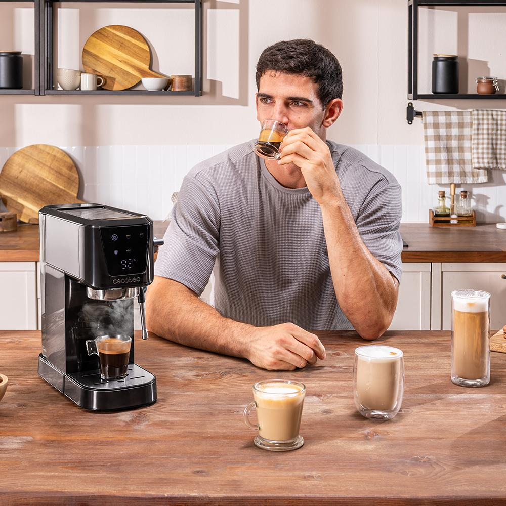Hombre bebiendo espresso. Cafetera a la izquierda. Tres bebidas de café en la mesa. Entorno de cocina con estantes y encimera de madera.