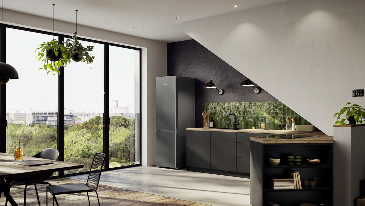 Moderne Küche mit dunklen Schränken, Kühlschrank und Esstisch. Große Fenster bieten einen Blick auf grüne Bäume und Gebäude.