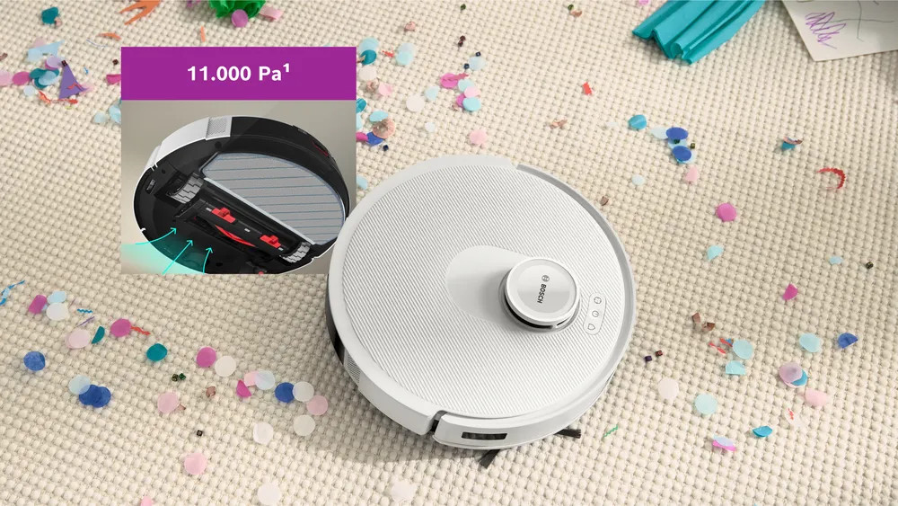 Biały odkurzacz automatyczny na dywanie pokrytym konfetti. Wstawka pokazuje elementy odkurzacza i tekst z liczbą 11.000 Pa.