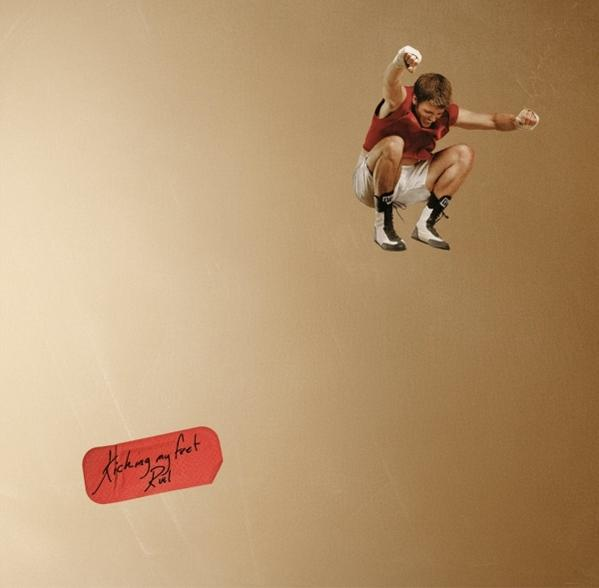 Ein Mann springt in die Luft, trägt eine rote Weste und weiße Shorts. Ein rotes Etikett sagt 'Kicking my feet'.
