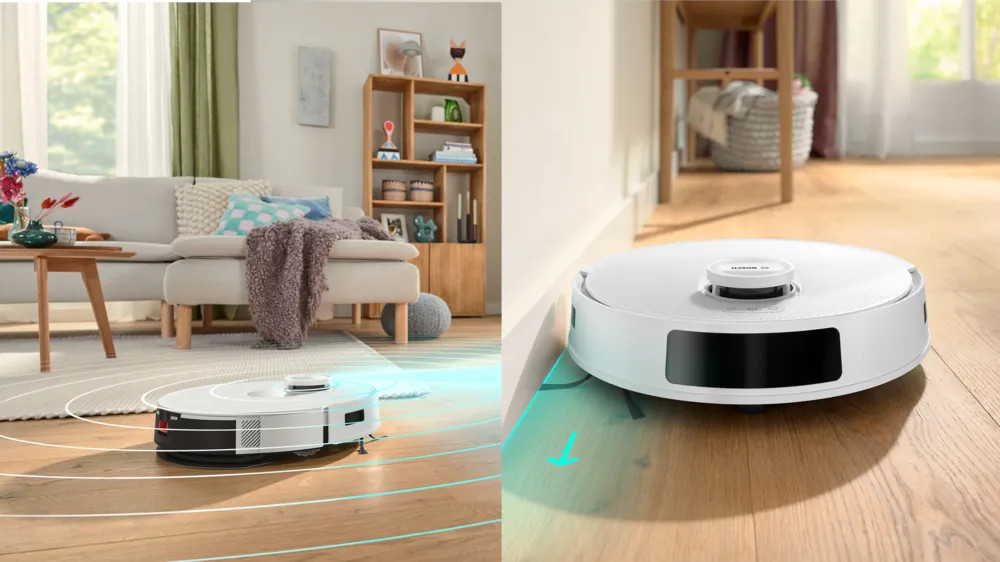 Biały odkurzacz robot sprząta pokój. Jest blisko sofy, stołu z kwiatami i drewnianej podłogi.