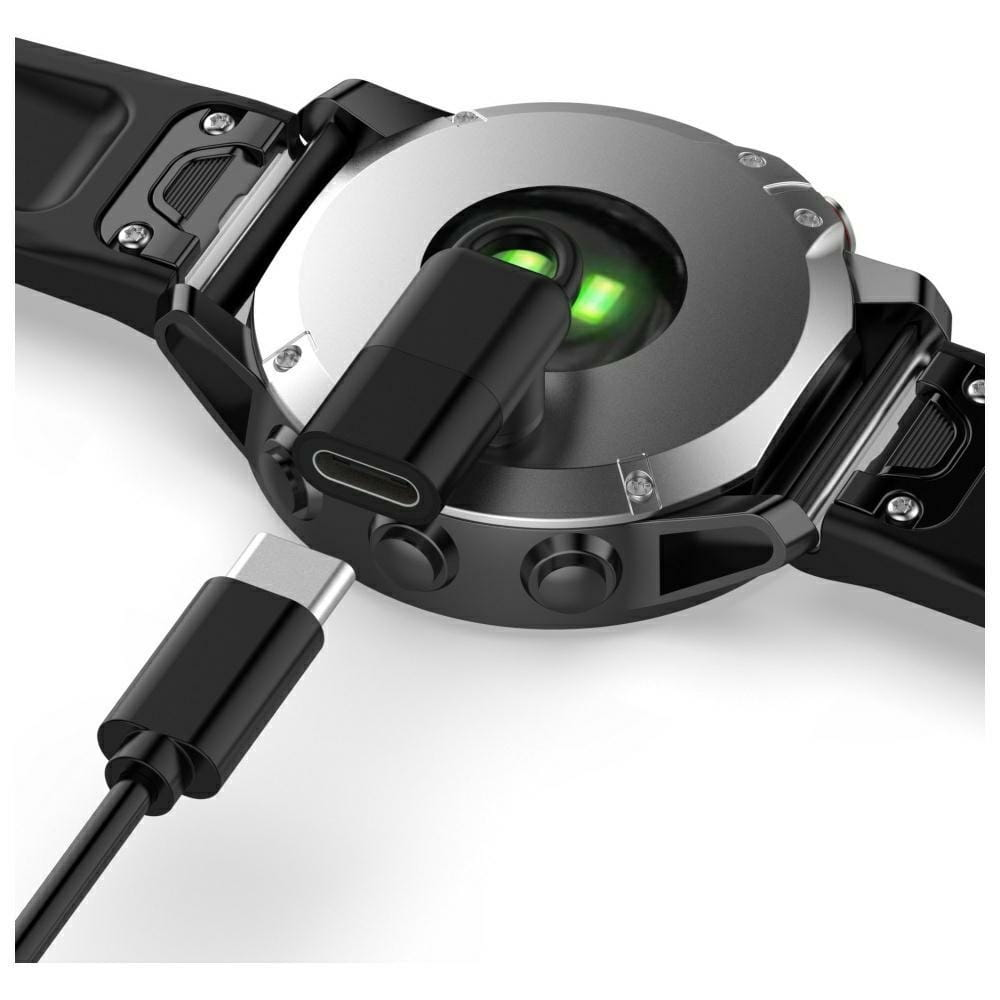 Czarny smartwatch z podłączonym kablem ładującym. Zegarek ma zielone światło, a ładowarka jest podłączona.