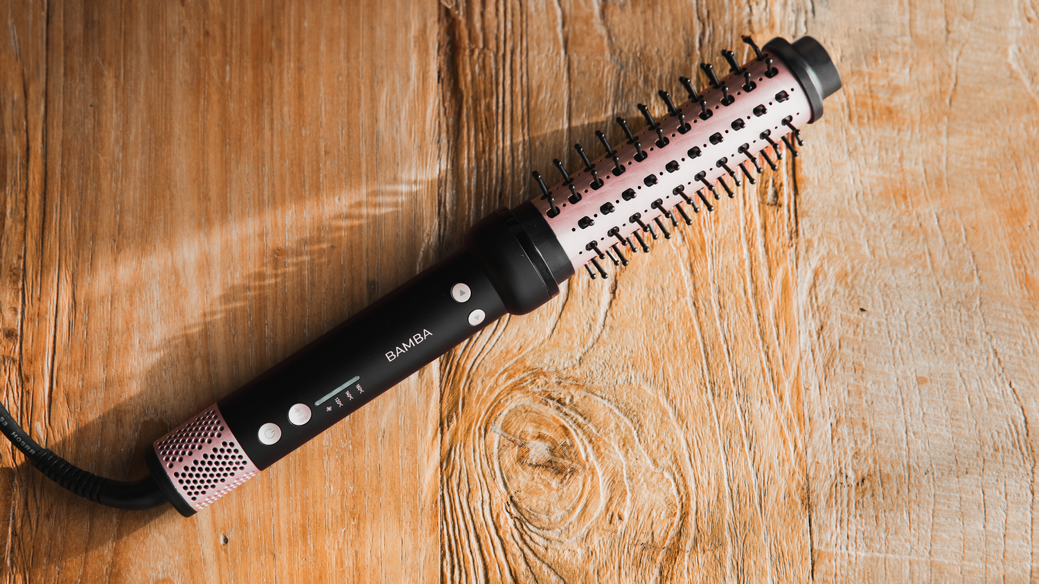 Un cepillo de peinado negro y rosa sobre una superficie de madera. El cepillo tiene la marca 'BAMBA'.