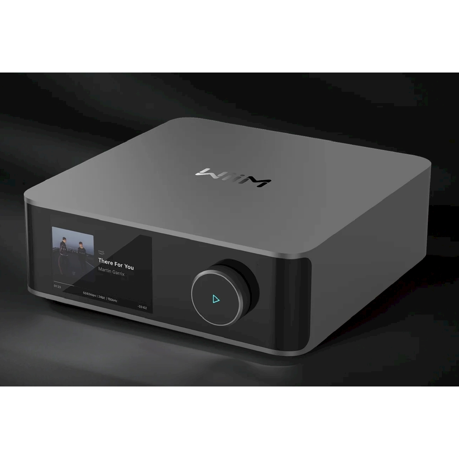 Un dispositivo audio grigio con schermo che mostra informazioni musicali e una manopola. È su una superficie scura e riflettente.