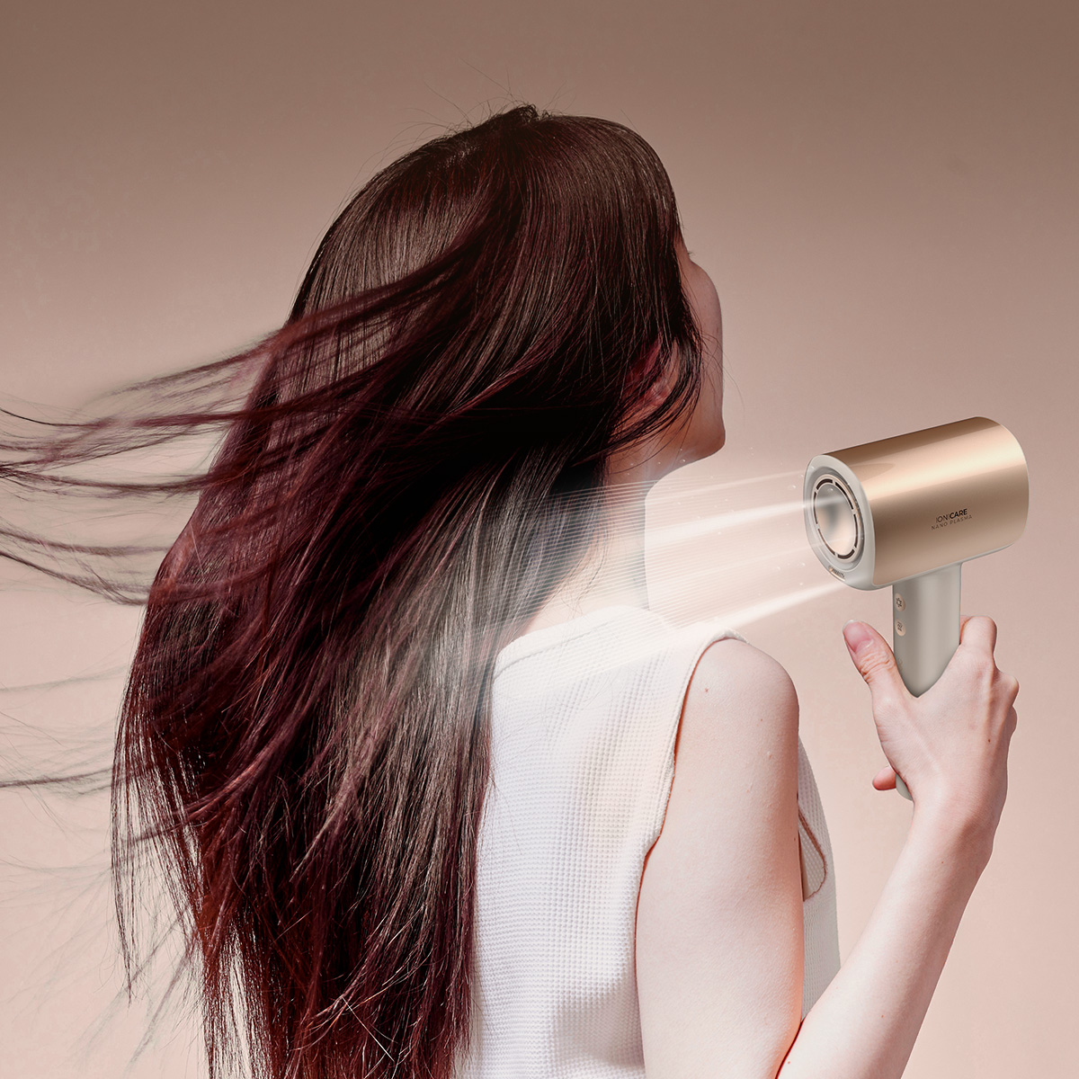 Mujer usando un secador de pelo dorado y blanco en su cabello castaño. El fondo es de color marrón claro.
