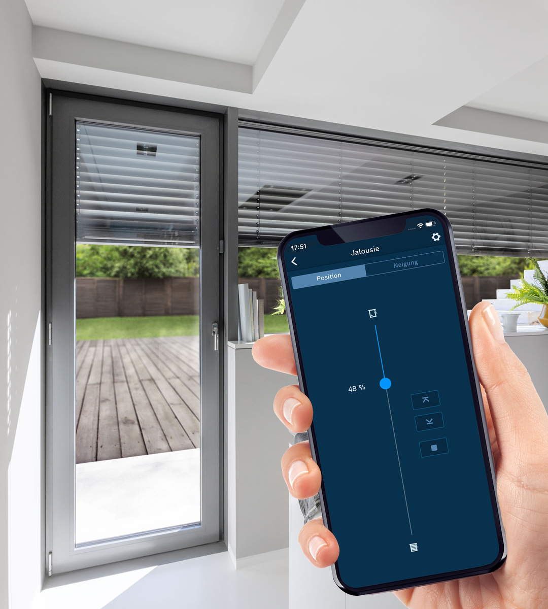 Eine Hand hält ein Smartphone, das Jalousien steuert. Der Bildschirm zeigt ein Bedienfeld. Im Hintergrund sind Jalousien und ein Fenster zu sehen.