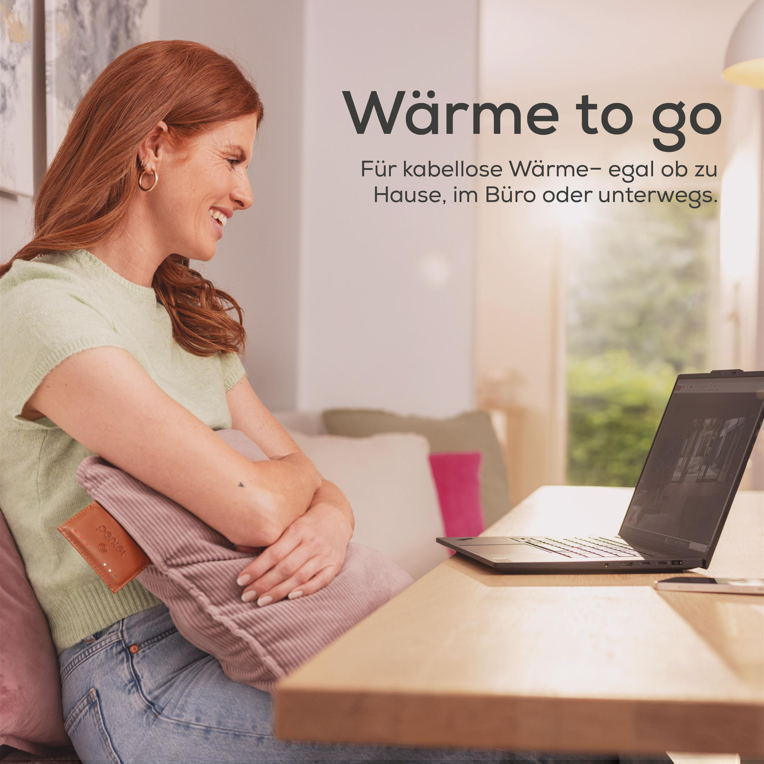 Rothaarige Frau lächelt, hält Kissen und schaut auf einen Laptop auf einem Holztisch.